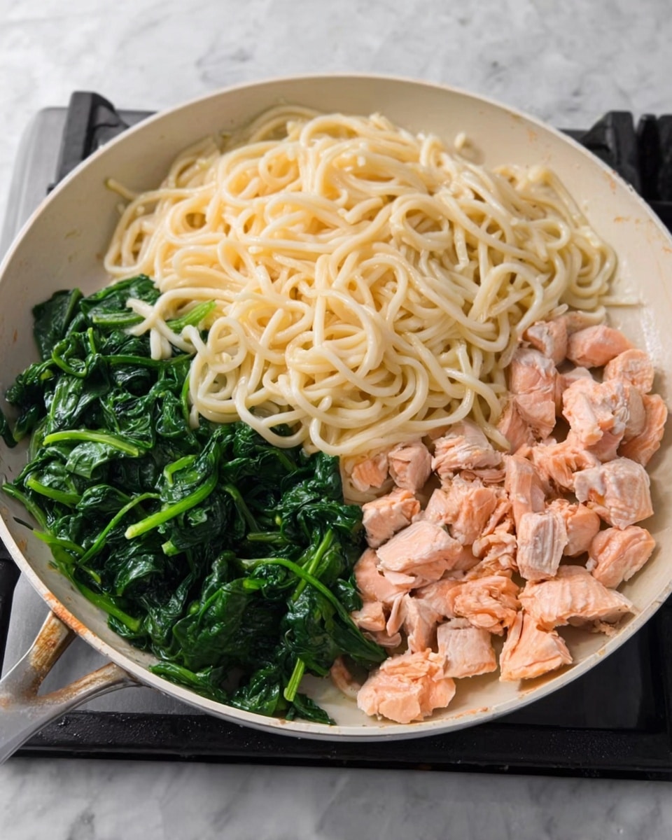 The image shows a white pan on a stove with three main parts: on the left side, there is a pile of thick, pale yellow noodles with a smooth texture; next to the noodles on the bottom and right side, bright green cooked spinach leaves with a slightly wet shine are placed; on the top right, chunks of cooked, light pink salmon pieces with a soft, flaky texture are arranged. The background is a white marbled surface. Photo taken with an iphone --ar 4:5 --v 7