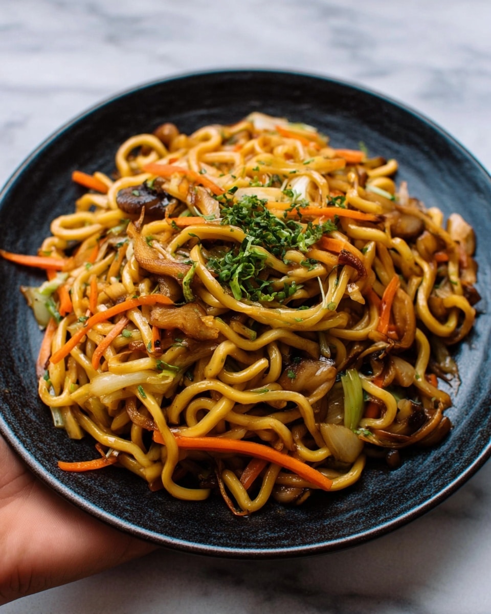 A close-up view of a black plate filled with a colorful stir-fried noodle dish. The dish has yellowish-brown thick noodles mixed with thin orange carrot strips, light brown mushrooms, and some green herbs sprinkled on top. The plate is placed on a white marbled surface, and a woman's hand is seen gently holding the edge of the plate from the side. photo taken with an iphone --ar 4:5 --v 7