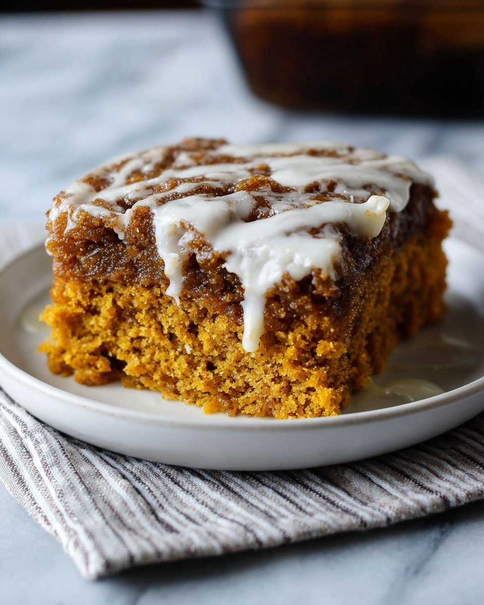 The image shows a rectangular glass baking dish filled with a warm dessert that has two main layers. The bottom layer is a soft, golden brown cake-like base, while the top layer is a crumbly, darker brown cinnamon streusel with irregular clumps. The whole dessert is drizzled with a thin, creamy white icing that runs down the crumbs and pools slightly at the edges. The dish is placed on a white marbled surface covered partially by a colorful cloth with stripes in orange, yellow, green, and red. The texture looks moist and inviting with a mix of smooth and crumbly parts photo taken with an iphone --ar 4:5 --v 7