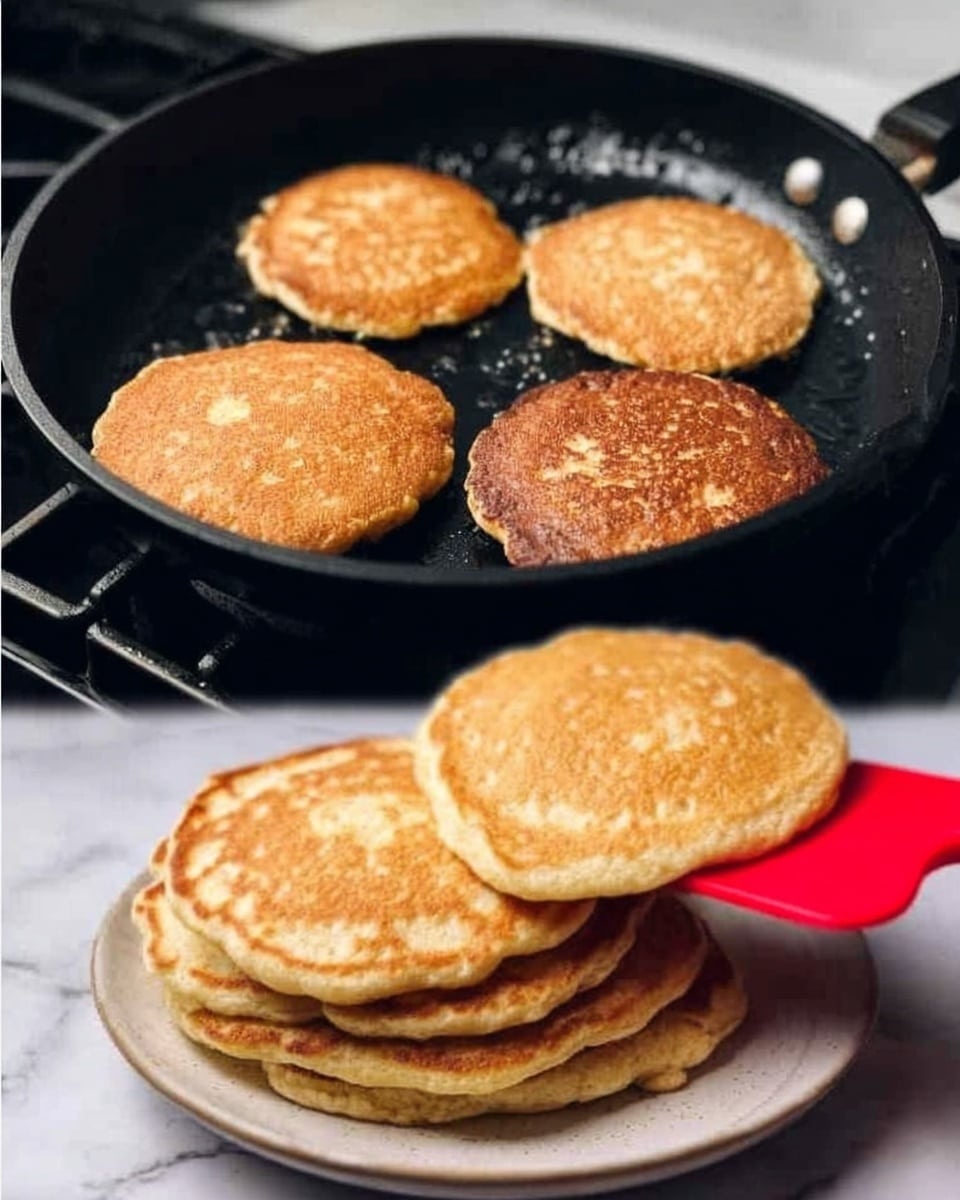 The image shows four golden brown pancakes cooking in a black frying pan on a stove. The pancakes have a round shape and a slightly uneven texture, showing small bubbles on their surface as they cook. Below the pan, there is a white plate filled with a stack of similar golden brown pancakes, with a red spatula lifting one pancake slightly to show its light, fluffy texture inside. The background features a white marbled kitchen surface. photo taken with an iphone --ar 4:5 --v 7
