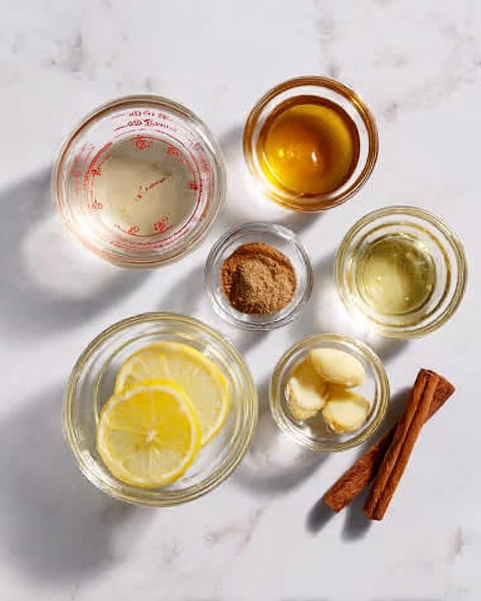 The image shows six small clear glass bowls arranged on a white marbled surface, each containing a different ingredient for a recipe. One bowl has a few round lemon slices stacked in clear liquid, placed near the bottom center. To the left, a bowl holds a pale measuring liquid with a red measurement marking, and next to it a bowl filled with golden honey. Above the lemon bowl are three smaller bowls with spices: one with a small pile of ground brown spice, one with a few whole clove spices, and one with light yellow oil. On the far right is a single cinnamon stick lying flat. The overall look is neat and organized with bright natural light, photo taken with an iphone --ar 4:5 --v 7