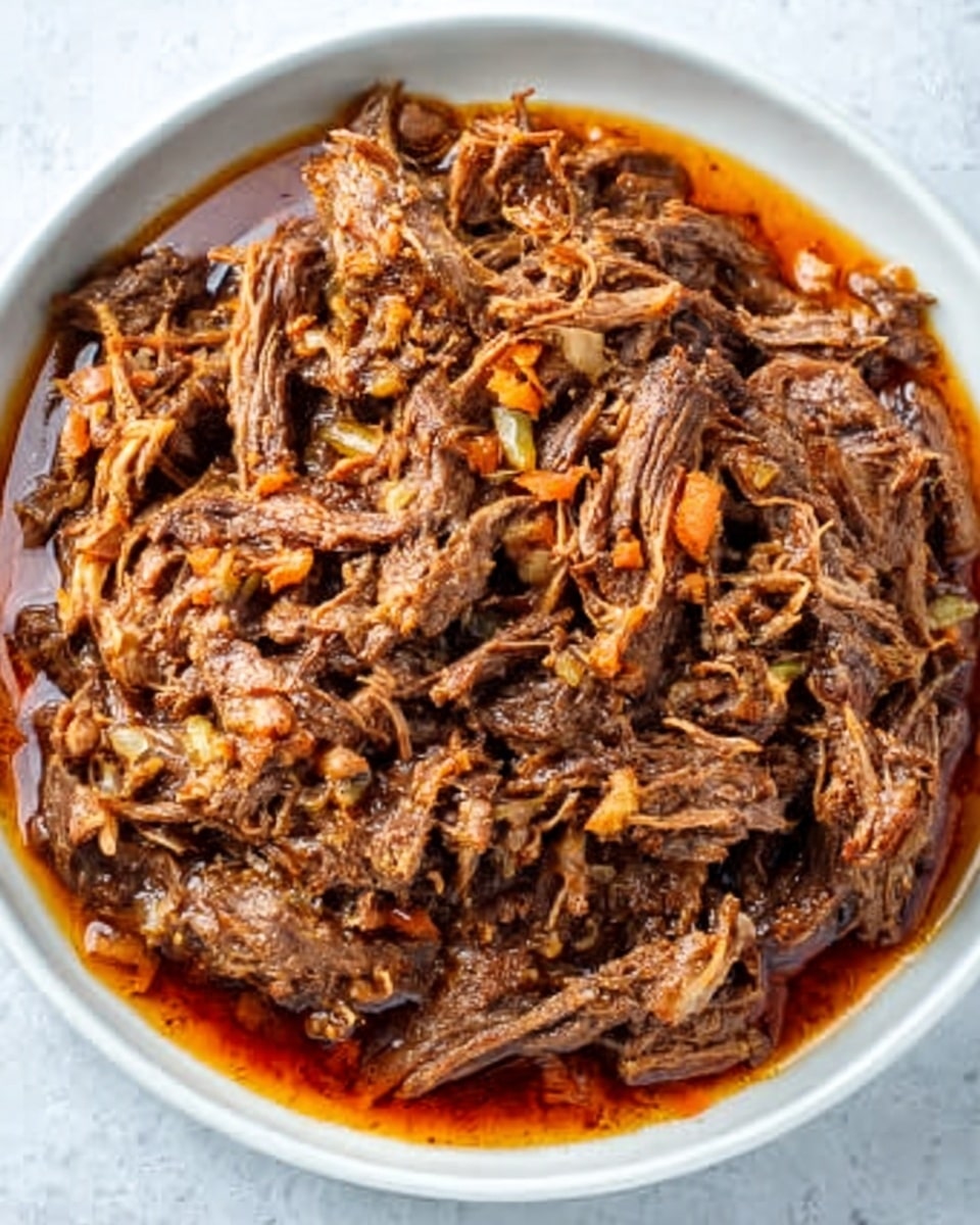 The image shows a clear white bowl filled with shredded cooked beef that looks tender and juicy. The beef is mixed with small pieces of cooked onion and bits of carrot, adding a touch of orange and off-white color among the deep brown meat. The beef sits in a thin layer of reddish-brown sauce that pools at the bottom right edge of the bowl. The white marbled surface under the bowl contrasts softly with the rich colors of the beef mixture. Photo taken with an iphone --ar 4:5 --v 7