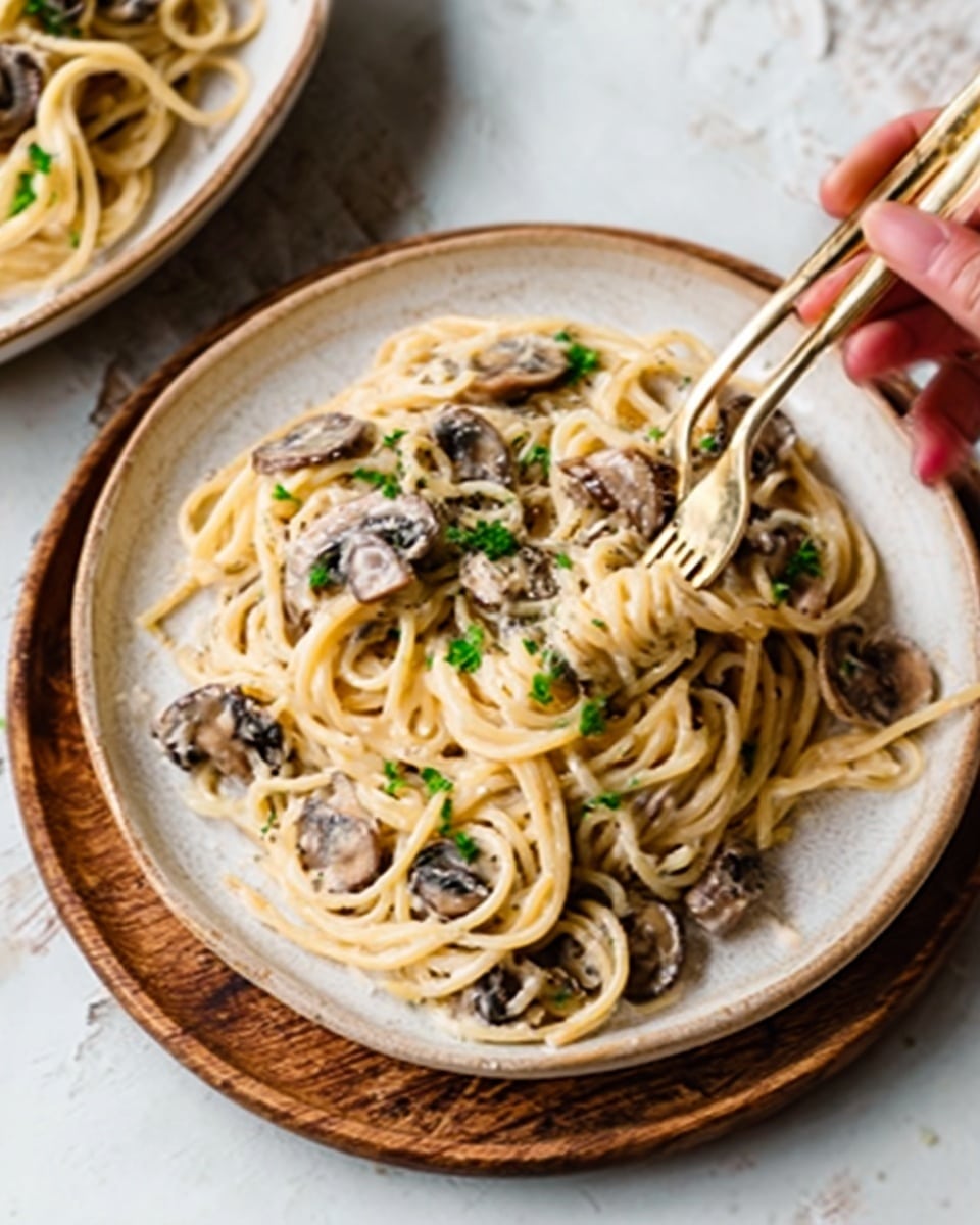 A white wooden plate holds creamy spaghetti mixed with sliced mushrooms and small bits of green herbs on top. The spaghetti is thick and coated in a light cream sauce, giving it a smooth texture with the mushrooms looking soft and slightly browned. A woman's hand is reaching in to grab some spaghetti with light colored utensils resting on the plate’s edge. In the background, another white wooden plate of similar spaghetti is partially visible. The surface under the plates is a white marbled texture. photo taken with an iphone --ar 4:5 --v 7