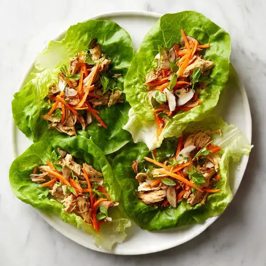 The image shows four lettuce wraps placed on a white plate on a white marbled surface. Each wrap has a large green lettuce leaf as the base, topped with a mix of shredded orange carrots, small white sliced mushrooms, and pieces of light brown cooked chicken. The textures include the crisp lettuce, soft chicken pieces, and fresh vegetables layered neatly. The leafy wraps are arranged evenly on the plate, creating a fresh and colorful presentation. photo taken with an iphone --ar 4:5 --v 7