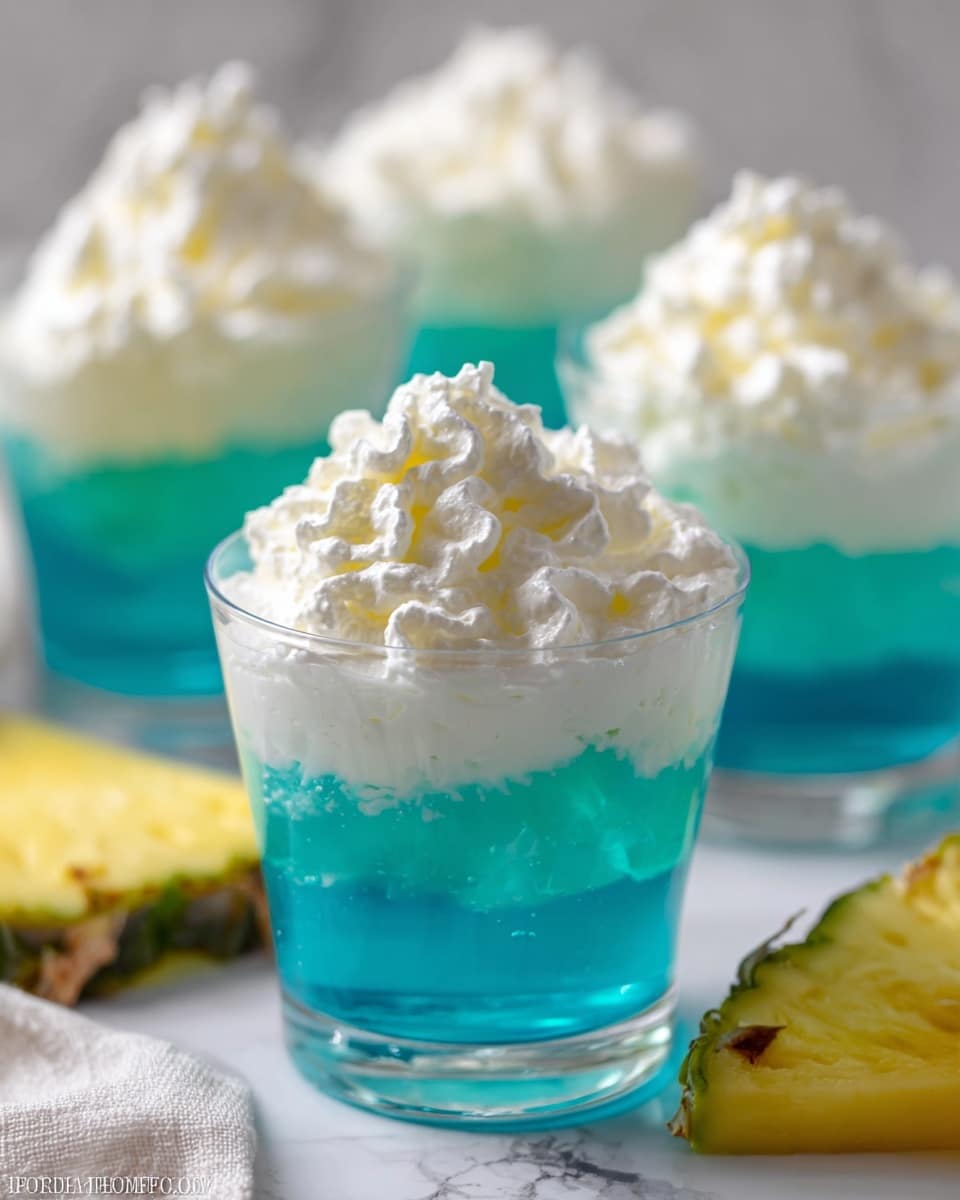 The image shows multiple clear short glasses filled with two layers: a bottom bright turquoise blue jelly layer with a smooth texture, and a thick, fluffy white whipped cream layer on top that is slightly textured and piled high. The glasses are set on a white marbled surface, and a yellow pineapple slice with a greenish edge lies in the foreground. The whipped cream has soft swirls and peaks, contrasting with the shiny, firm blue jelly beneath it. The overall look is fresh and vibrant with the bright blue and white colors standing out. photo taken with an iphone --ar 4:5 --v 7