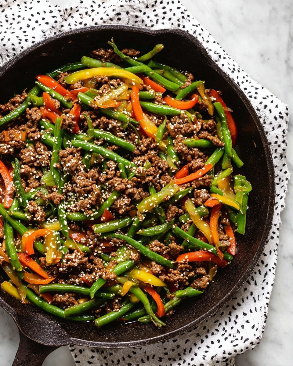 A black cast iron pan is filled with a colorful stir fry featuring three main layers: bright green beans cut into small sections, thin orange carrot sticks, and yellow bell pepper slices, all mixed with chunks of browned ground meat coated in a shiny sauce. The vegetables appear fresh and slightly glossy, mixed evenly with the meat, which looks tender and juicy. White sesame seeds are sprinkled on top, adding a light texture and color contrast. The pan rests on a white cloth with a simple dark pattern and is set on a white marbled surface. photo taken with an iphone --ar 4:5 --v 7