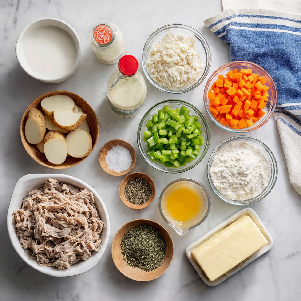 The image shows a neat arrangement of cooking ingredients on a white marbled surface. There are eleven bowls and containers in total: a large white bowl with shredded light brown meat in the center bottom, to the left a white bowl with round slices of light pink potatoes, and nearby a clear bottle of light beige liquid with a red cap. Above these are clear bowls with chopped green bell peppers, green celery, white flour, bright orange diced carrots, and a white bowl with finely chopped or grated onions. Four small wooden bowls hold different dried green herbs and black pepper, while a small wooden bowl with white salt sits near the center. Also present is a small clear bowl of melted yellow butter and a clear jug with white milk at the top center. A stick of butter with measurement marks lies to the right bottom. A blue and white striped cloth is partially visible at the top edge. Photo taken with an iphone --ar 4:5 --v 7