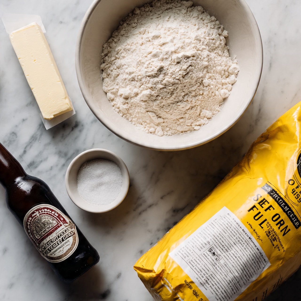 The image shows baking ingredients placed on a white marbled surface. There is a large white bowl filled with a light, powdery white flour in the top center of the image. To its right, a bright yellow bag of self-rising flour leans against the bowl, with black and white text on it. In front of the bowl, a stick of pale yellow butter wrapped in paper lies flat. To the left of the butter, a small white round dish filled with white granulated sugar is visible. On the far left, a brown beer bottle with a detailed label in red, white, and black colors stands upright, adding a dark contrast to the light tones of the other ingredients. Photo taken with an iphone --ar 4:5 --v 7