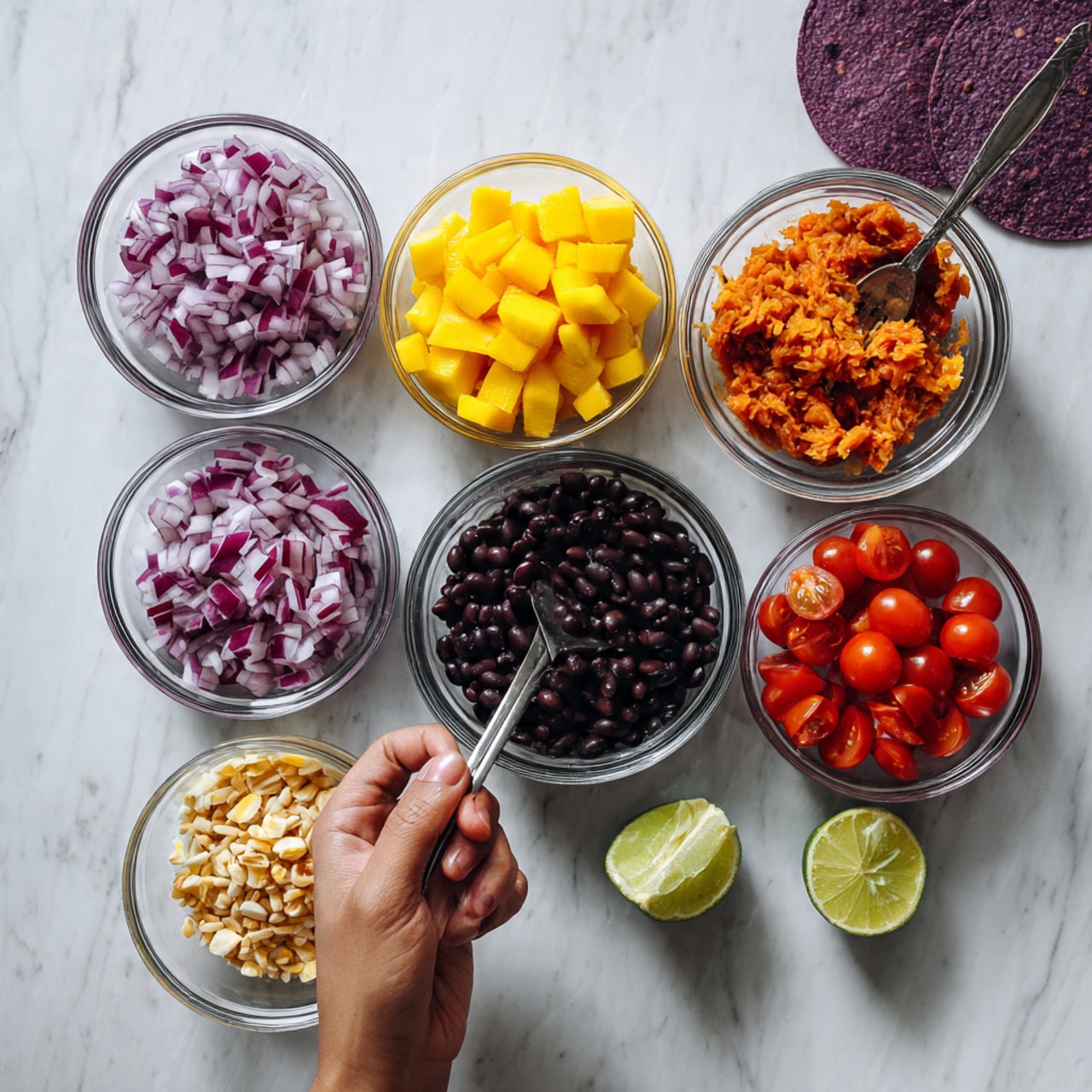 The image shows six small clear bowls arranged on a white marbled surface. Starting from the top left, there are chopped red onions in one bowl, bright yellow diced mango pieces in the top middle bowl, and a reddish-orange mashed mixture in the top right bowl. In the bottom left bowl, there are small crushed peanuts or garlic pieces; in the center bowl, there are black beans; and in the bottom middle bowl, there are quartered red cherry tomatoes. A wedge of lime sits near the bottom right, and two purple corn tortillas are partially visible on the left side. A woman's hand holding a fork is seen at the top right corner of the photo taken with an iphone --ar 4:5 --v 7