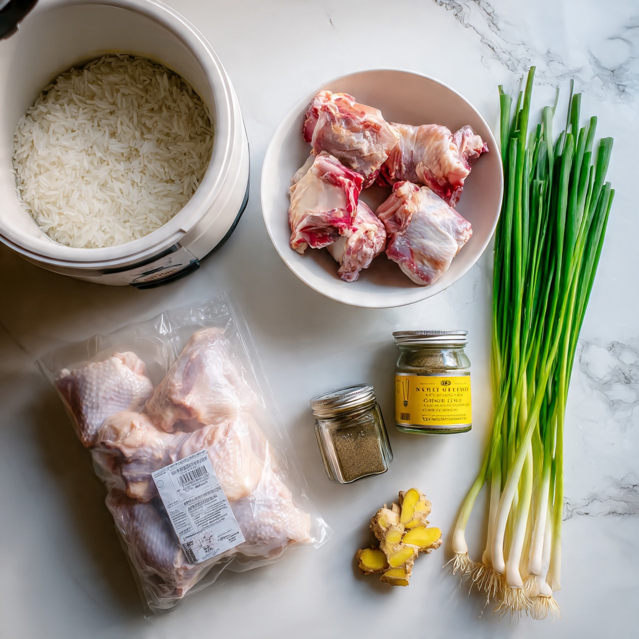 The image shows a top view of raw ingredients arranged on a white marbled texture. On the left side, there is a white rice cooker filled with uncooked rice, appearing white and slightly translucent. Next to it is a white bowl filled with three pieces of raw chicken bones with pale pink and red hues, showing some blood and texture. Below the bowl, a vacuum-sealed pack of pale pink chicken drumsticks is visible with a label on it. Beside the pack are two small jars, one of chicken stock concentrate with a yellow label and the other a spice jar with a clear lid. Finally, a bunch of fresh green onions with deep green tops and white bulbs is placed diagonally across the bottom right of the image. A small piece of yellow ginger is on the bottom right corner. Photo taken with an iphone --ar 4:5 --v 7