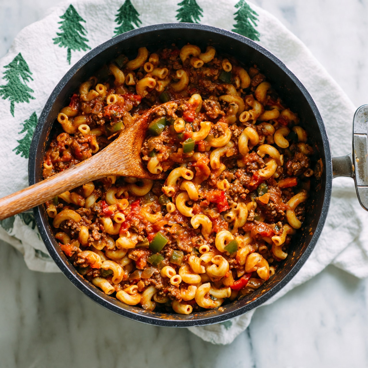 A black cooking pot filled with macaroni pasta mixed with a chunky red tomato sauce, ground meat, small pieces of green and red bell peppers, and diced onions, all combined evenly throughout the dish. The elbow-shaped pasta is pale yellow and soft looking, blending with the rich, thick sauce covering every layer. A wooden spoon is resting inside the pot, scooping up some of the pasta and sauce mixture, with the pot sitting on a white marbled surface next to a white cloth with a green tree pattern. Photo taken with an iphone --ar 4:5 --v 7
