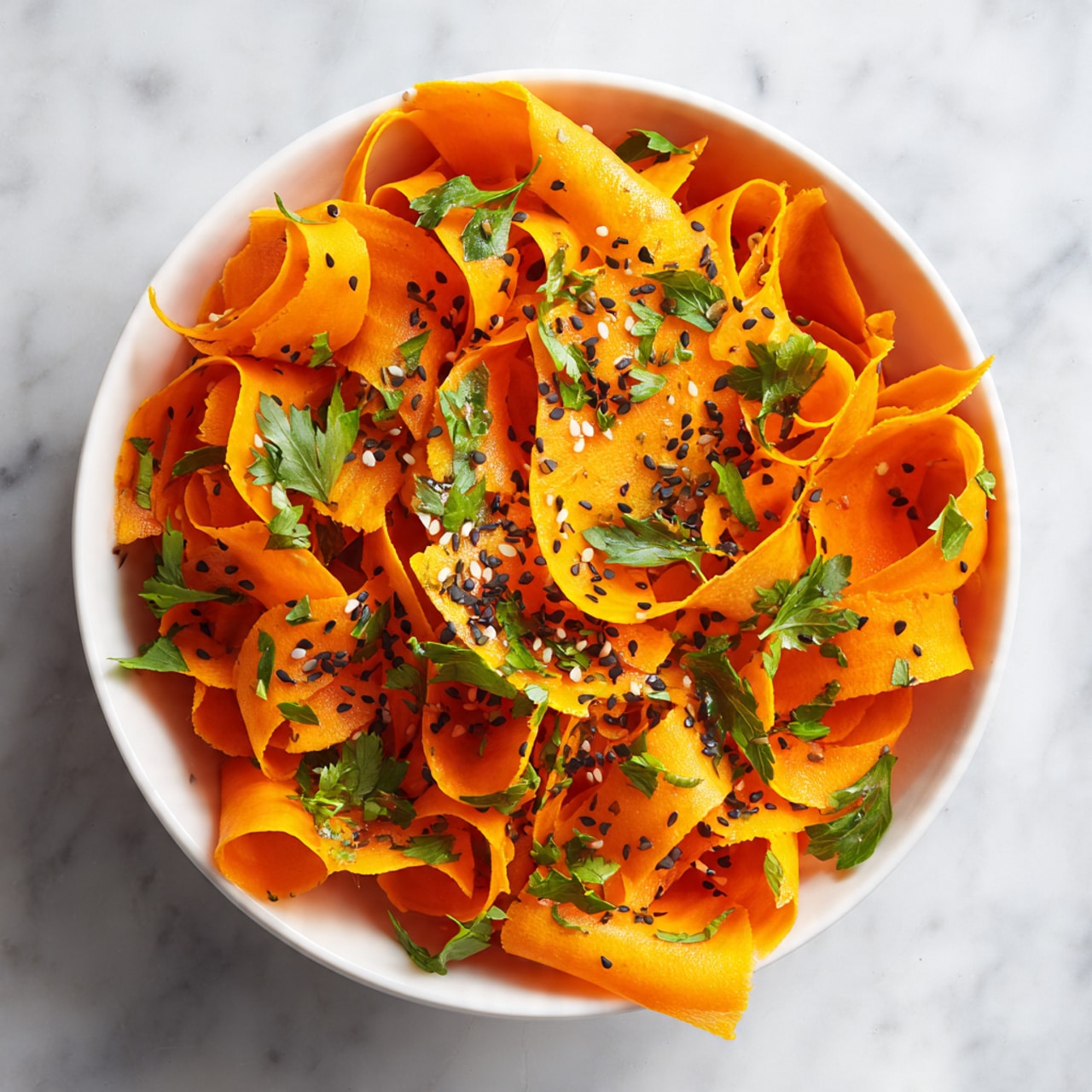 This image shows a close-up of a carrot salad made of several thin, curled strips of bright orange carrot layered loosely in a bowl. Each carrot strip curls in different directions, creating soft, ribbon-like folds and waves with a slightly glossy texture. Scattered on top are small black and white sesame seeds, adding contrast with their smooth, round shapes. Fresh green parsley leaves are sprinkled throughout, their rough, jagged edges and leafy texture brightening the orange. The bowl is white, sitting on a white marbled surface that is mostly out of focus. photo taken with an iphone --ar 4:5 --v 7