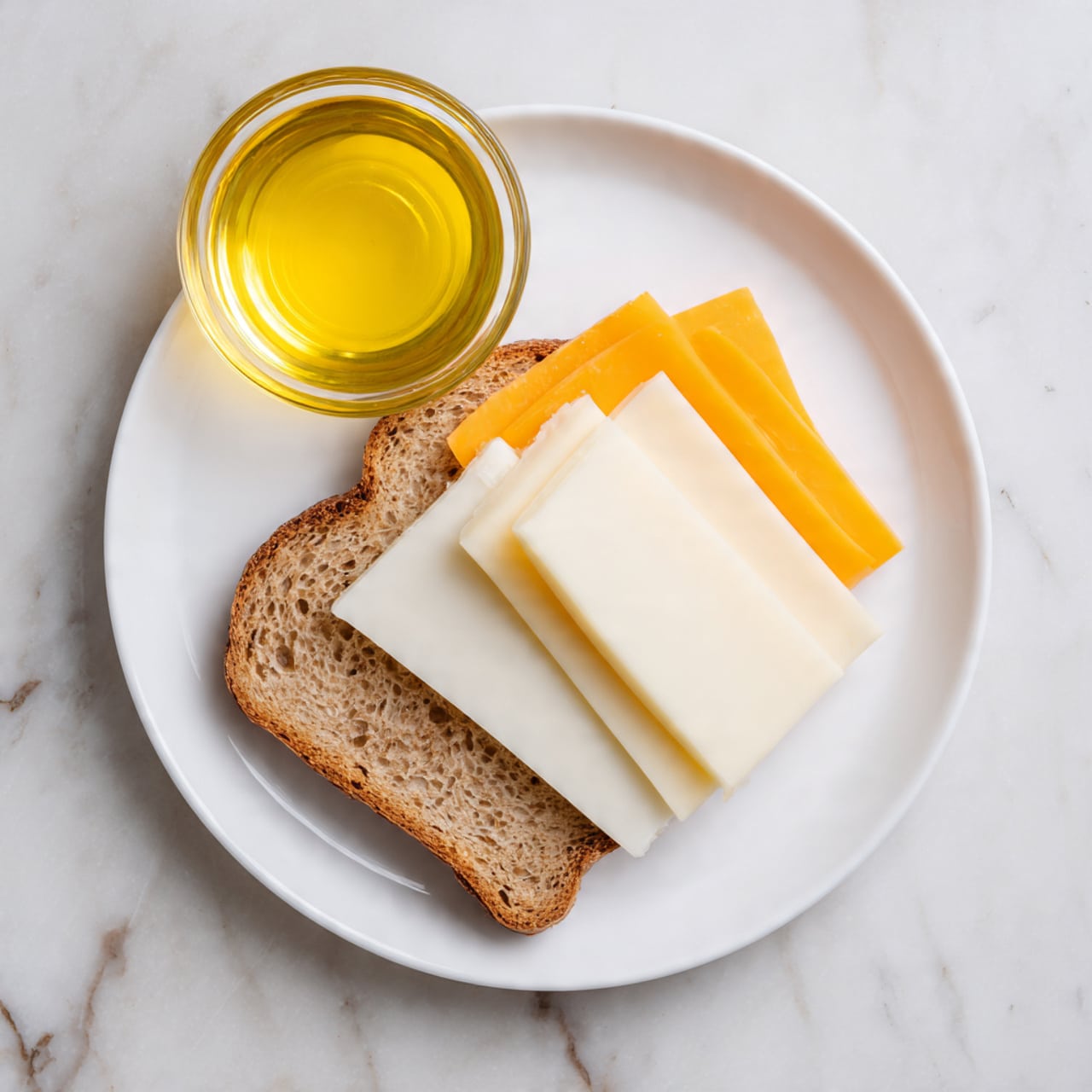The image shows a white plate with one slice of light brown bread placed near the bottom edge. On top of the bread, there are three slices of cheese closely stacked: one white slice on the left, another white slice in the middle, and a yellow-orange slice on the right, creating a layered effect. Above the plate, there is a small glass bowl filled with bright yellow liquid. The whole scene is set on a white marbled surface. photo taken with an iphone --ar 4:5 --v 7