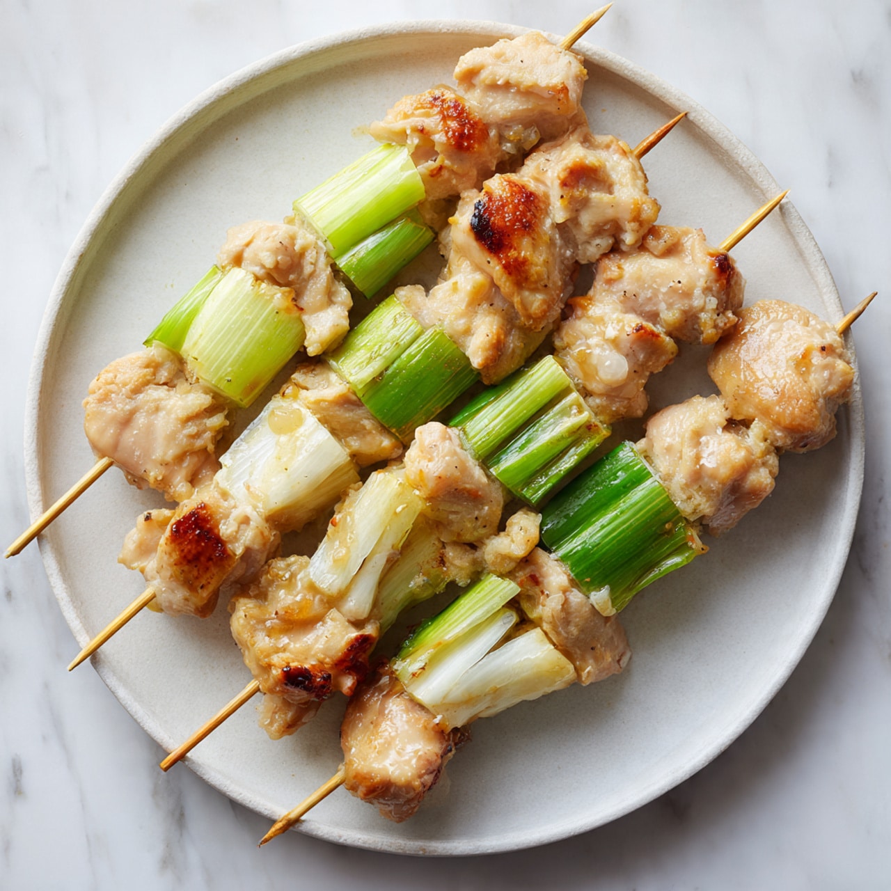 A round white metal plate holds five skewers laid out side by side on a white marbled textured surface. Each skewer has chunks of light brown marinated raw chicken meat mixed with small bits of garlic, alternating with thick sections of pale green and white parts of green onions. The chicken pieces look moist and soft with a slightly shiny texture, while the green onions add fresh, smooth, and stiff layers, creating a simple and fresh look for the skewers. photo taken with an iphone --ar 4:5 --v 7