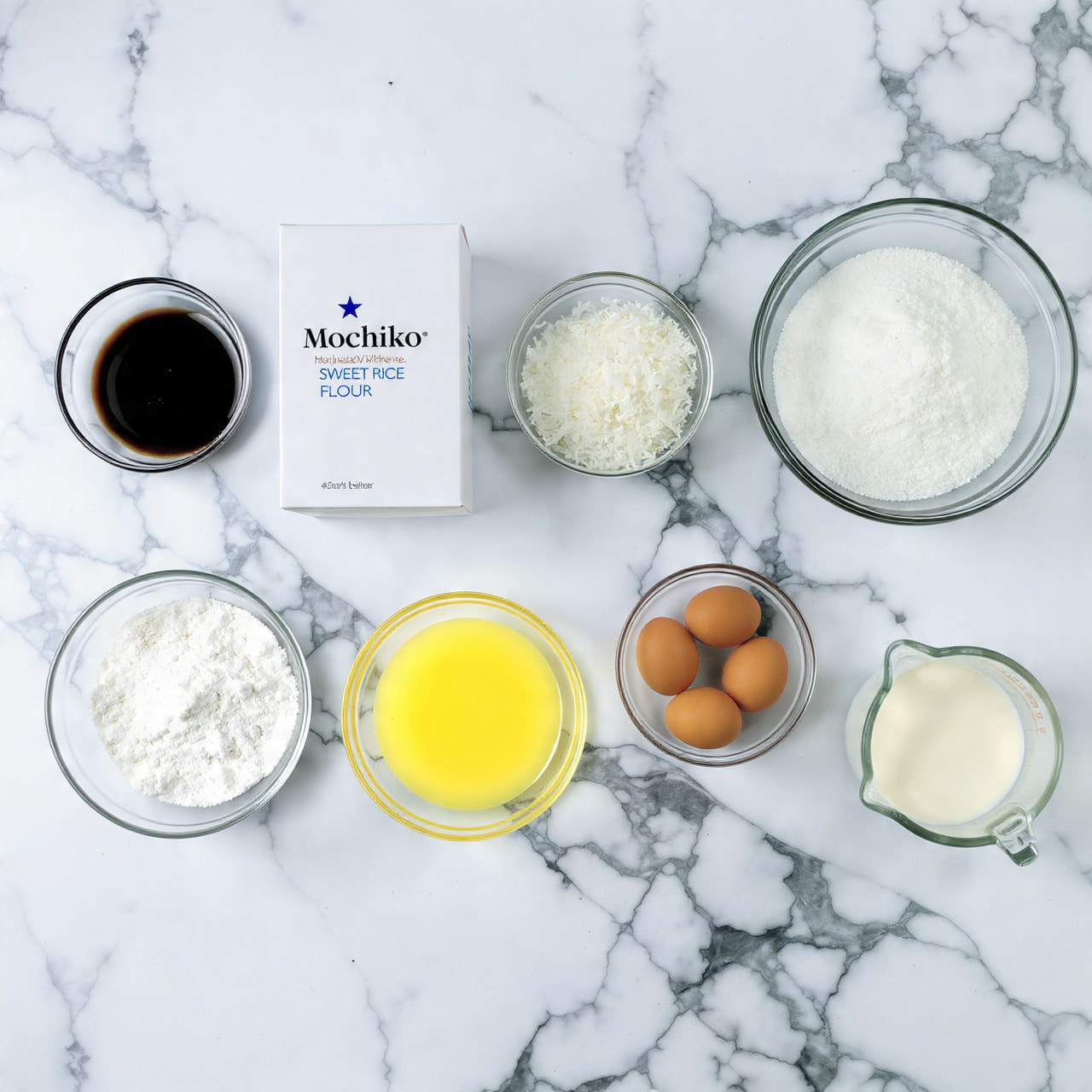 On a white marbled surface, there are seven separate clear glass bowls and one white box arranged neatly. The top row shows a small bowl with dark brown liquid on the left, next to a tall white box labeled