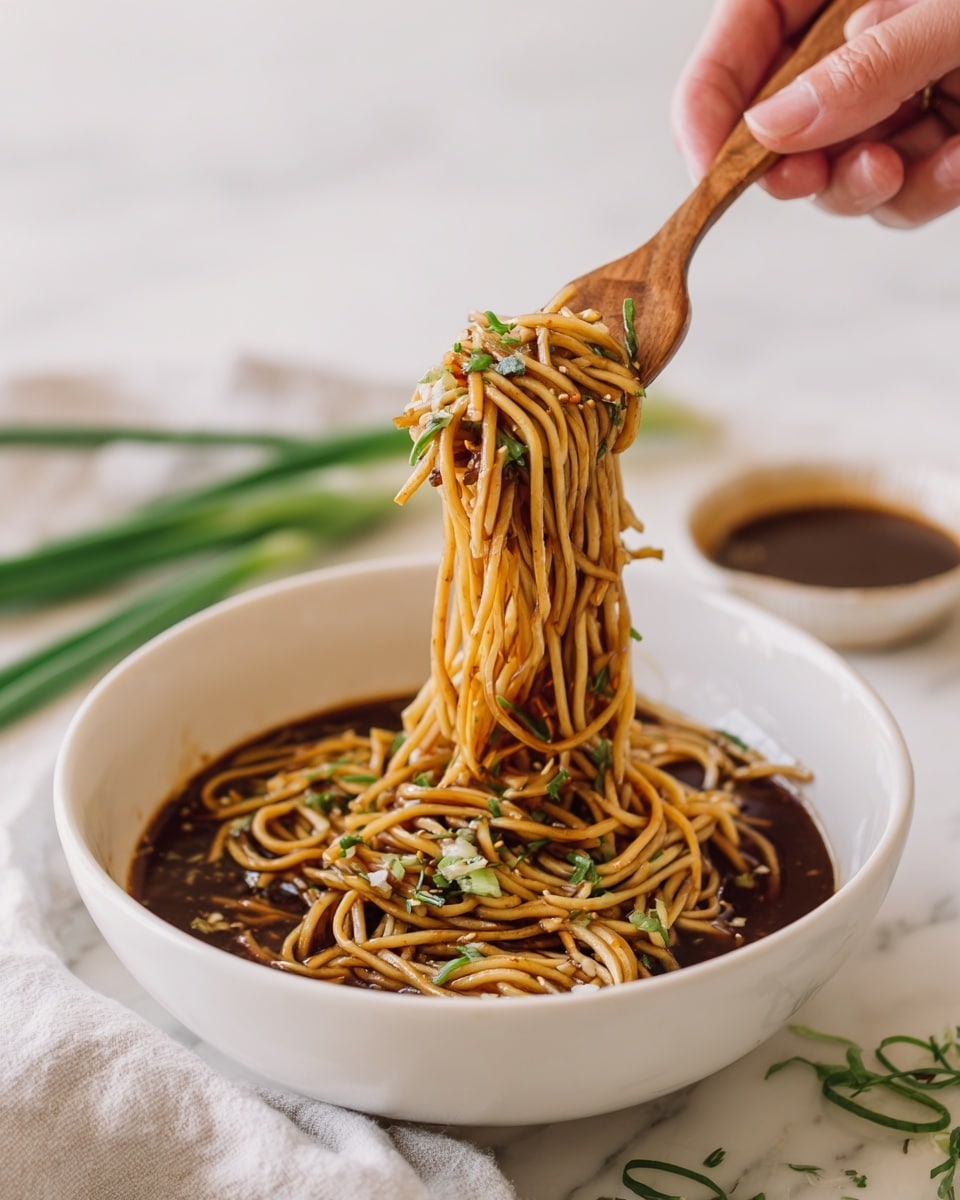 A white bowl filled with cooked noodles covered in dark brown sauce, with small pieces of green herbs sprinkled on top. Woman's hand holding a wooden fork lifts a portion of the noodles, showing their long, soft texture. The bowl sits on a white marbled surface with green onion stalks and a white saucer with sauce blurred in the background. Photo taken with an iphone --ar 4:5 --v 7