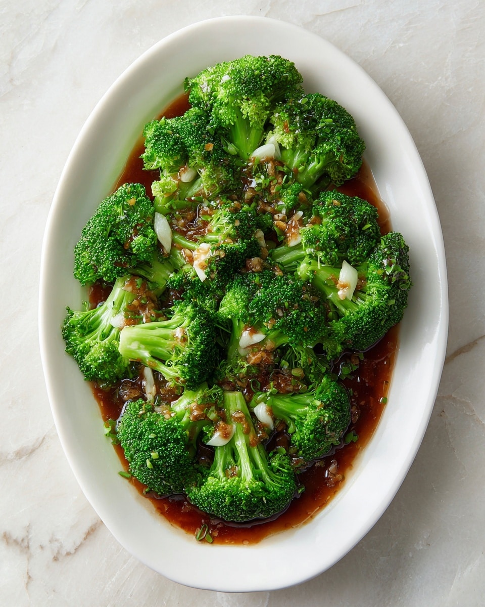 A white oval plate holds a bed of bright green broccoli florets, arranged in a circular pattern along the edges and around the center. On top, there is a deep brown sauce with a shiny texture that spreads over the broccoli, containing small pieces of pale-colored garlic scattered within it. The plate is placed on a white marbled textured surface, creating a clean and fresh look. Photo taken with an iphone --ar 4:5 --v 7