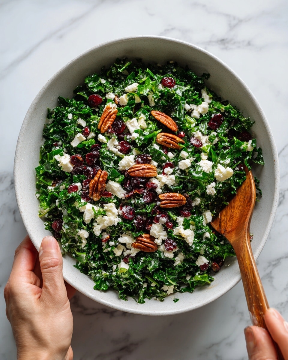 The image shows a fresh salad in a white bowl placed on a white marbled surface. The salad has one main layer of finely chopped green kale leaves filling the bowl. Scattered on top are small white chunks of cheese, dark red dried cranberries, and whole brown pecans. A woman's hand holds a wooden fork resting inside the bowl near the edge. The colors are mostly green with white, red, and brown accents, giving a fresh and healthy look. Photo taken with an iphone --ar 4:5 --v 7