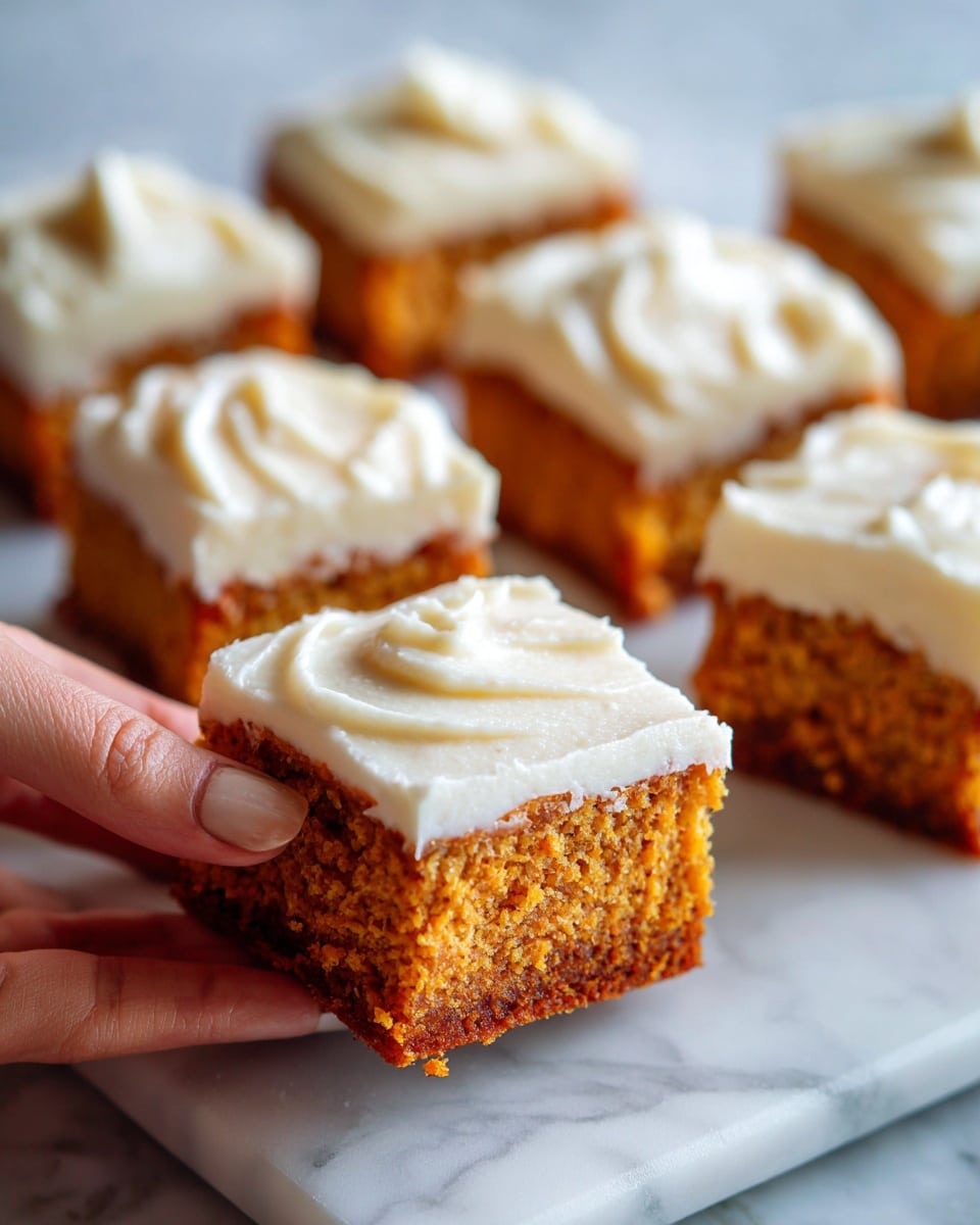 The image shows several square pieces of pumpkin cake with a smooth layer of creamy white frosting on top. Each cake piece has one thick layer of orange-brown cake at the bottom and one thick layer of light, creamy frosting on top. The frosting has a soft texture with visible gentle swirls. The cake pieces are placed on a white marbled surface, and the focus is on one piece in the center, with a woman's hand gently holding its side. The photo taken with an iphone --ar 4:5 --v 7