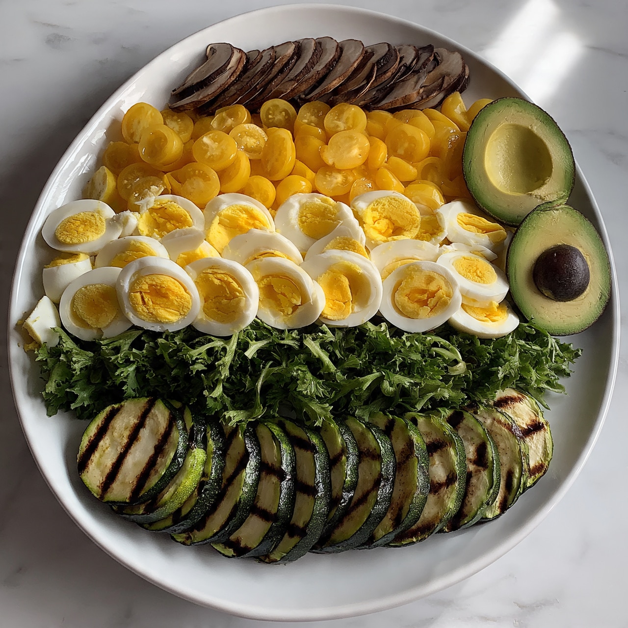 square image A white oval plate on a white marbled surface holds a colorful salad with several layers. At the bottom, there are grilled zucchini slices with dark grill marks, placed in a row. Above the zucchini, small green lettuce leaves make a fresh bed across the plate. On top of the greens, a layer of halved yellow cherry tomatoes is spread evenly. Sliced boiled eggs with bright yellow yolks and white edges are arranged over the tomatoes, with some pieces near the side. Thin slices of brown mushrooms are placed near the top edge of the plate. On one side of the plate, two avocado halves with green flesh and dark seed inside are placed carefully. The whole dish is vibrant with fresh vegetable textures and colors. photo taken with an iphone --ar 4:5 --v 7