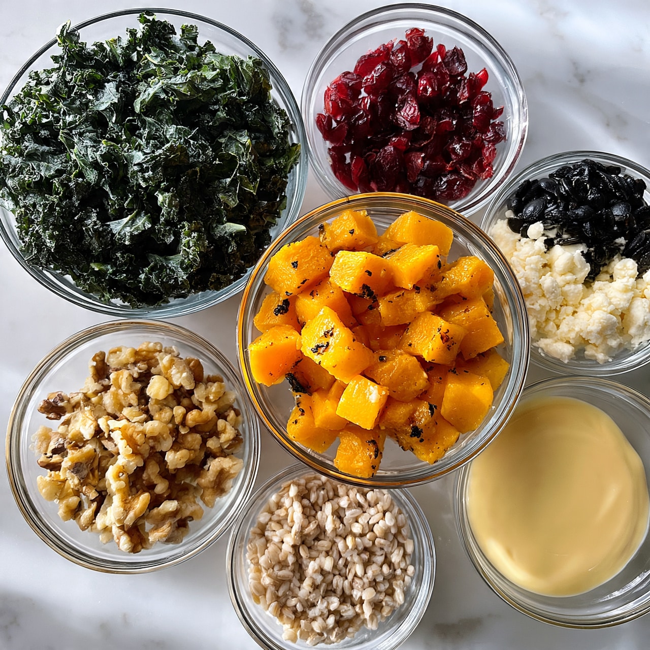 square image Several clear glass bowls are placed on a white marbled surface, each holding different ingredients for a salad. The largest bowl at the top left is filled with chopped dark green kale leaves with a rough texture. At the center is a medium bowl of orange-yellow roasted butternut squash cubes with a slightly soft texture and some dark seasoning spots. Smaller bowls surround these, including red dried cranberries, crumbled white cheese, black roasted pumpkin seeds, chopped light brown walnuts, light beige barley grains, and a pale yellow creamy dressing. The bowls are arranged neatly with clear visibility of each ingredient’s color and texture. Photo taken with an iphone --ar 4:5 --v 7