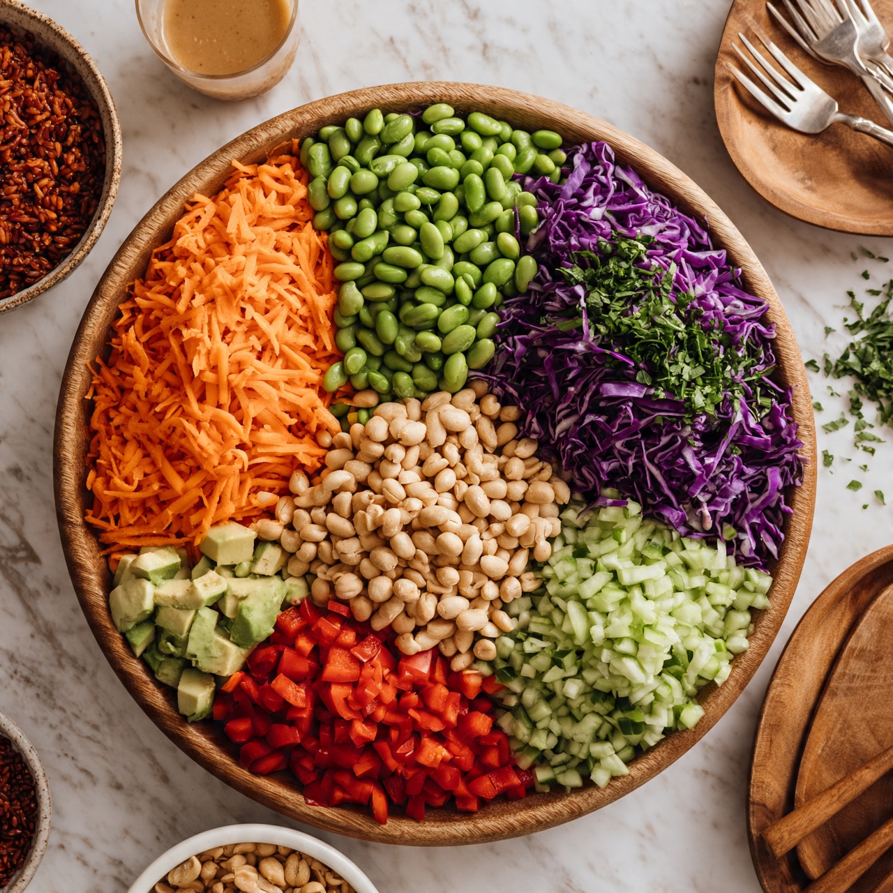 square image A large wooden bowl filled with a colorful salad arranged in sections: bright orange shredded carrots at top left, fresh green edamame beans next to it, deep purple shredded cabbage with chopped green herbs on top at top right, and light green chopped cucumbers below that. At the center pile, there are pale brown peanuts. At the bottom left, there are small pieces of light green avocado and bright red chopped bell peppers. The bowl sits on a white marbled surface with a glass of light brown dressing above it, a bowl of red rice to the left, and a white bowl of peanuts near the bottom. On the right side, there is a wooden bowl with three forks. Some green herbs are scattered around. Photo taken with an iphone --ar 4:5 --v 7
