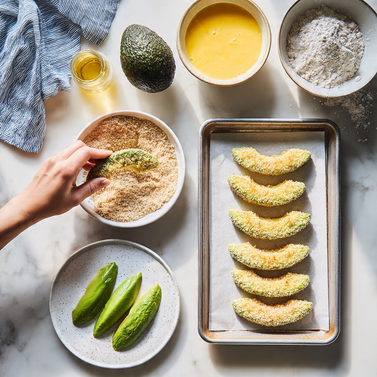 square image The image shows a food preparation scene on a white marbled surface with several white bowls and plates. In the center-left, a woman's hand is dipping a green avocado slice coated in breadcrumbs into a bowl full of light brown breadcrumbs. Below, a white speckled plate holds three bright green avocado slices with smooth texture. To the right, a metal tray lined with parchment paper displays nine avocado slices already breaded, arranged in three rows. Above the bowls and plates, from left to right, a small glass jar contains a yellow liquid, a whole dark green avocado with a rough skin, a bowl with a smooth yellow beaten egg mixture, and another bowl filled with white flour with some scattered on the edge. A blue and white striped cloth is folded to the top left of the frame. The lighting is bright and natural, highlighting the colors and textures. photo taken with an iphone --ar 4:5 --v 7
