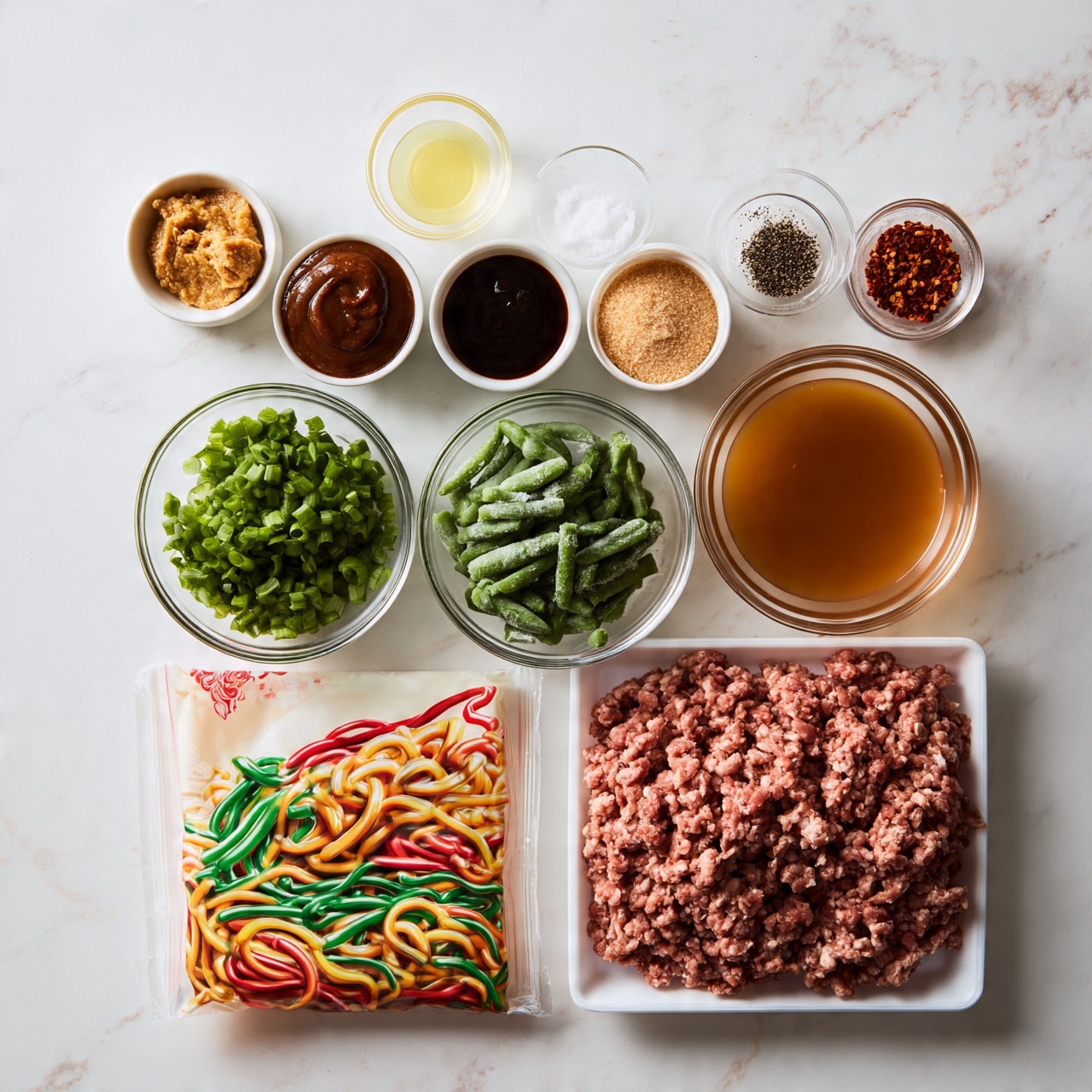 square image The image shows a clean white marbled surface with ingredients neatly arranged. At the bottom right, there is a white tray filled with raw ground meat. Next to it on the left, there is a package of udon stir-fry noodles with colorful noodles pictured on the front. Above the noodles and meat, there are two clear glass bowls side by side, one filled with fresh green chopped scallions and the other with frozen green beans. To the right of these, there is a clear glass bowl filled with a light brown liquid. Above these bowls, three small white bowls hold thick dark brown sauce, another dark sauce, and light brown sugar. Above the sugar, to the left, is a small clear glass bowl with a yellow liquid. Around this are four small bowls: one white bowl with golden brown paste, two small clear glass bowls holding white powder and ground black pepper, and one holding red pepper flakes. Everything is organized neatly in rows and columns, photographed with an iphone --ar 4:5 --v 7