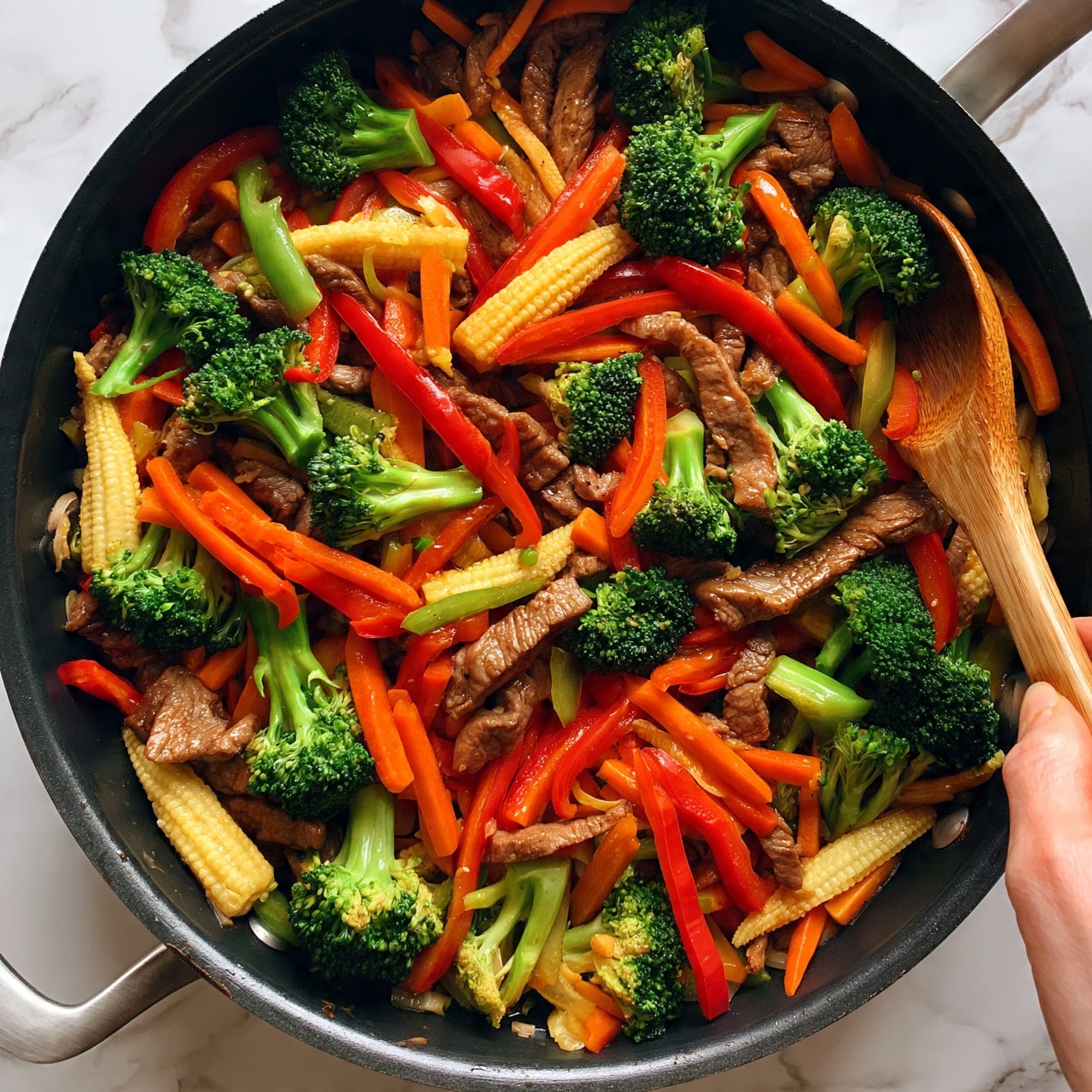 square image A large black frying pan filled with a colorful stir-fry of vegetables and thin strips of cooked meat. The dish has bright green broccoli florets, many thin red bell pepper strips, orange carrot slices, and light yellow baby corn pieces spread evenly throughout. The meat is mixed in well, showing a brownish color and a tender texture. A wooden spoon is resting in the pan, being held by a woman's hand. The pan sits on a white marbled surface. The photo taken with an iphone --ar 4:5 --v 7