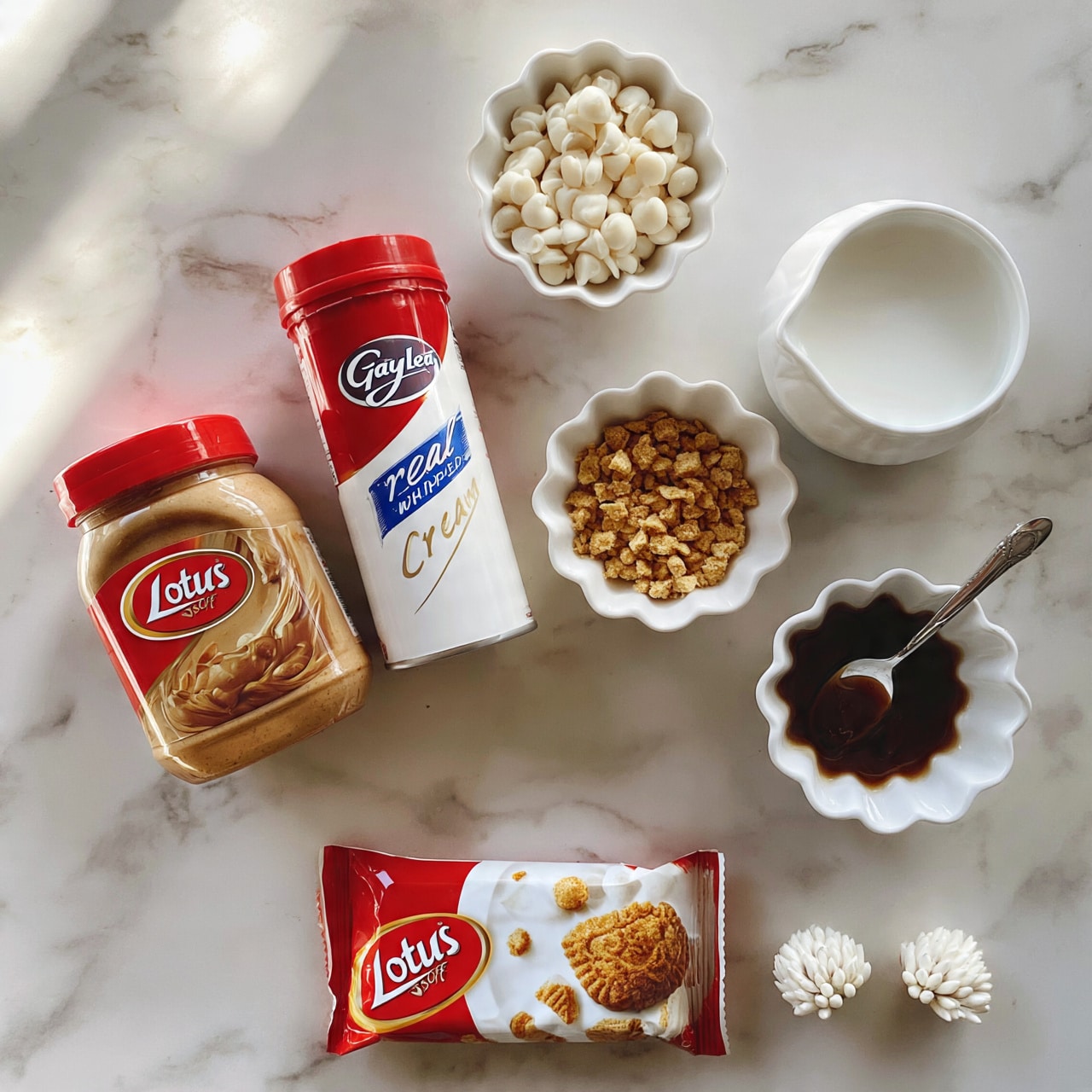 square image The image shows six items placed on a white marbled surface: a jar of Lotus Biscoff spread with a red lid on the left, a can of Gay Lea real whipped cream with a red top standing upright next to it, a small white scalloped bowl filled with white chocolate chips above, a white ceramic container holding a white liquid to the right, another white scalloped bowl filled with small golden brown crunchy bits below the chocolate chips, and a smaller white scalloped bowl containing a spoon with dark sticky syrup. At the bottom, there is a closed red and white Lotus Biscoff cookie package and two small white decorative flower buds to the right. photo taken with an iphone --ar 4:5 --v 7