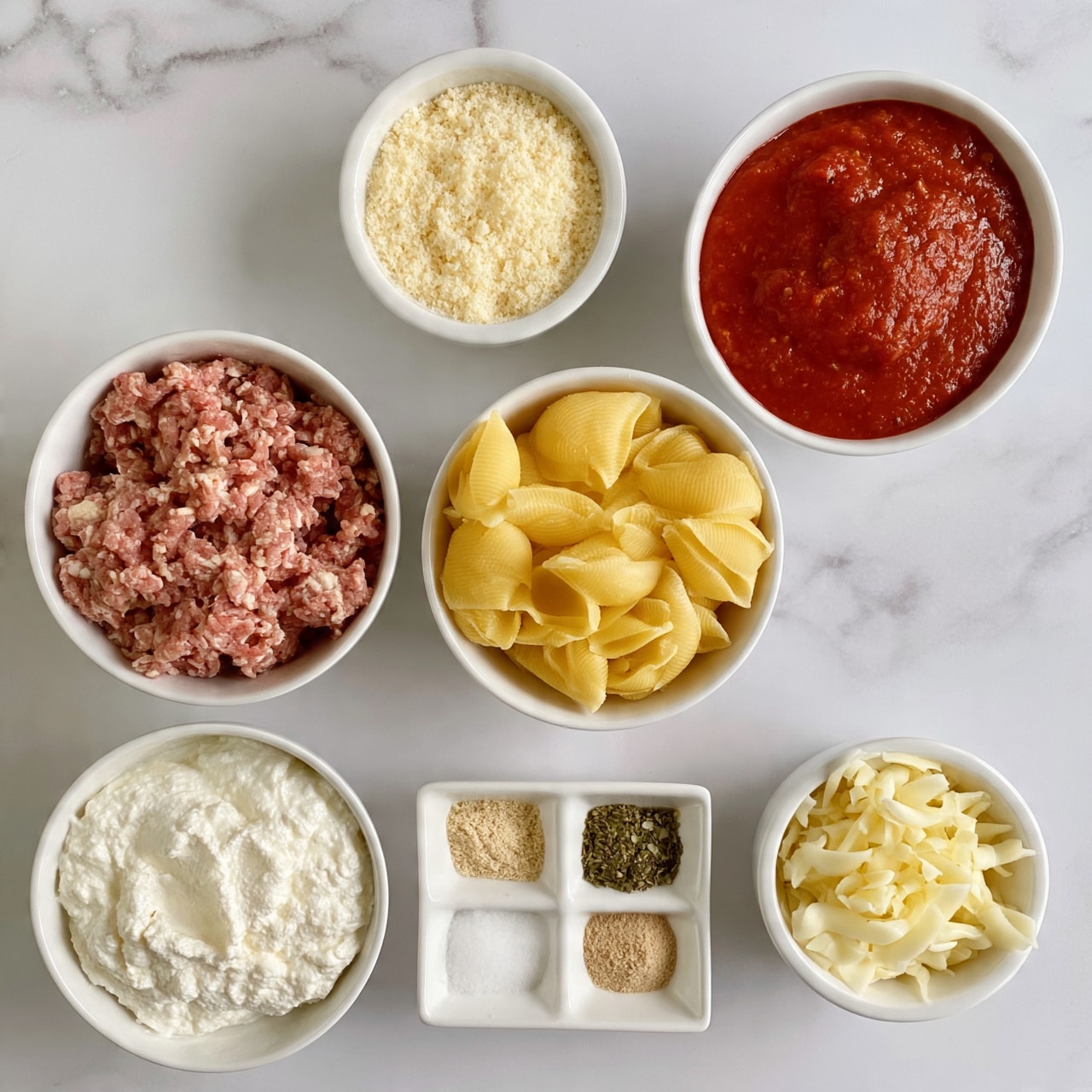 square image The image shows seven bowls arranged on a wooden surface, each containing different ingredients for a meal. At the top center, a small white bowl holds grated light yellow cheese. To its right, a medium white bowl is filled with thick, smooth red tomato sauce. Below, a medium white bowl contains yellow pasta shells with a hard texture. On the left, a medium white bowl is filled with pink ground meat with a coarse texture. Below that is another medium white bowl with smooth white ricotta cheese. Near the bottom left, a white tray holds four small compartments with finely ground beige powder, salt, a green herb mix, and light brown powder. At the bottom right, a small white bowl contains shredded pale yellow mozzarella cheese. The surface is changed to a white marbled texture. photo taken with an iphone --ar 4:5 --v 7