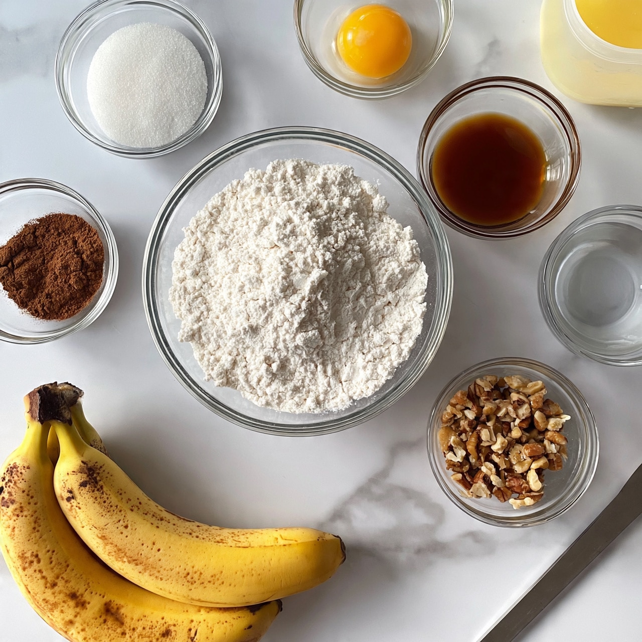 square image The image shows several ingredients placed on a white marbled surface, ready for baking. There are two ripe bananas with brown spots at the bottom left, next to a clear glass bowl filled with white flour in the center. Around the flour bowl are smaller clear glass bowls holding white sugar, a raw egg yolk in the center, dark brown cinnamon powder, brown liquid (likely vanilla), chopped nuts, and a small bowl of water. To the far right is a clear container with melted butter. A metal tool is partially visible at the bottom right, close to the butter. Photo taken with an iphone --ar 4:5 --v 7
