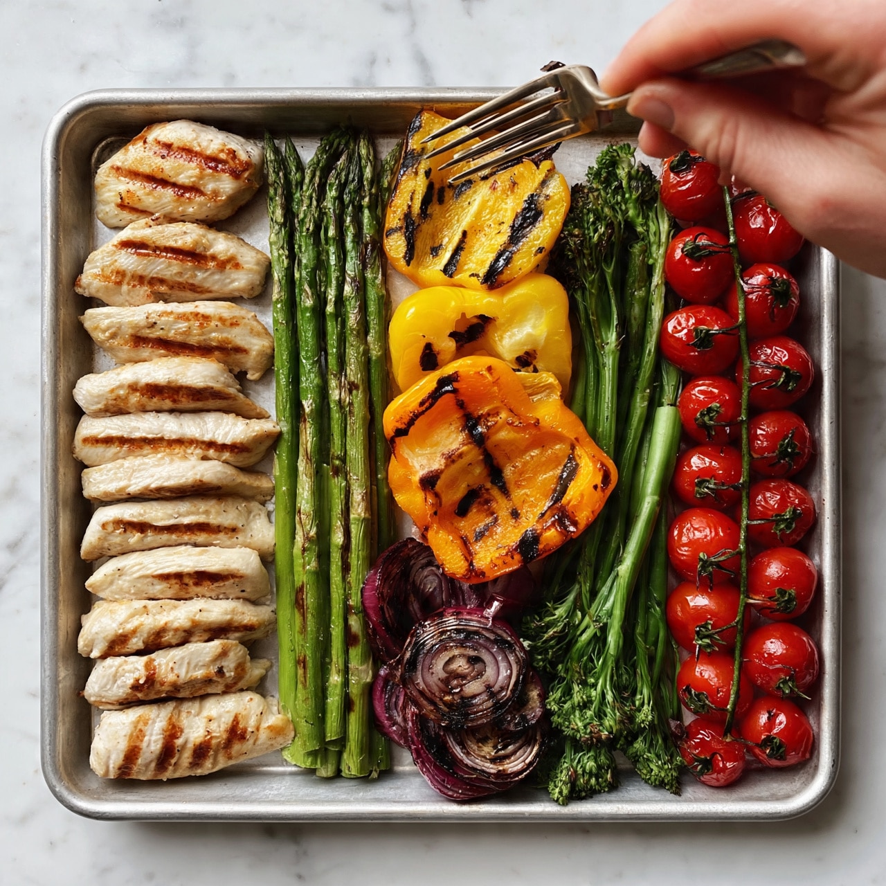 square image The image shows a rectangular metal tray filled with grilled food, placed on a white marbled surface. On the left side, there are 6-7 light golden grilled chicken strips with clear grill marks, beside a neat row of green grilled asparagus with slight char lines. Next to the asparagus is a small pile of grilled red onion slices with dark grill rings. In the middle, there are bright grilled yellow and orange bell pepper halves with visible black grill marks. To the right of them are green grilled broccolini stalks. On the far right side, bright red grilled cherry tomatoes still on the vine create a colorful line. A woman's hand is holding a fork on the top right corner of the tray. The photo taken with an iphone --ar 4:5 --v 7
