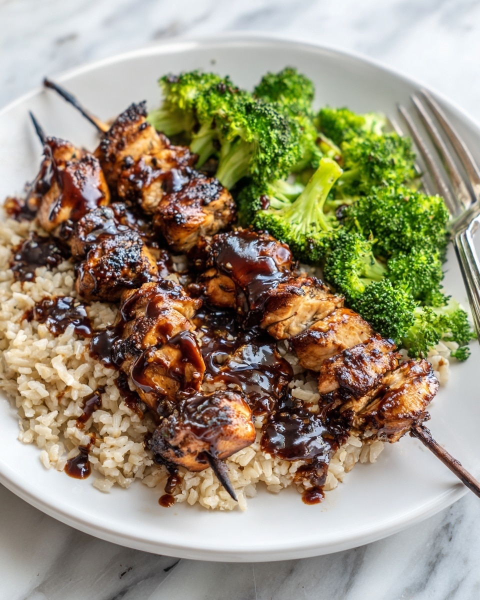 A white plate holds a meal with three skewers of grilled chicken coated in shiny dark brown sauce. The largest skewer is in the middle, flanked by a medium skewer on the left and a smaller skewer on the right, all placed on a bed of light brown rice forming the bottom layer. To the right side of the plate, bright green broccoli florets with a fresh, slightly bumpy texture are arranged next to the skewers. A silver fork rests behind the broccoli at the edge of the plate, and the plate is set on a white marble textured surface. photo taken with an iphone --ar 4:5 --v 7