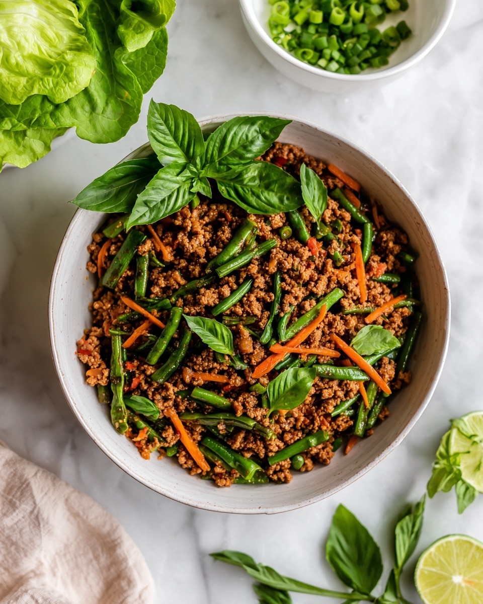 A white bowl is filled with a mix of cooked ground meat with small carrot sticks and green beans mixed in, giving a colorful look of brown, bright orange, and green. The dish is topped with fresh green basil leaves. Around the bowl, there are pieces of fresh lettuce, a wedge of lime, and some green herbs arranged on a white marbled surface. In the background, a white bowl with chopped green onions is partially visible, along with a woman's fingers holding a piece of lettuce. photo taken with an iphone --ar 4:5 --v 7