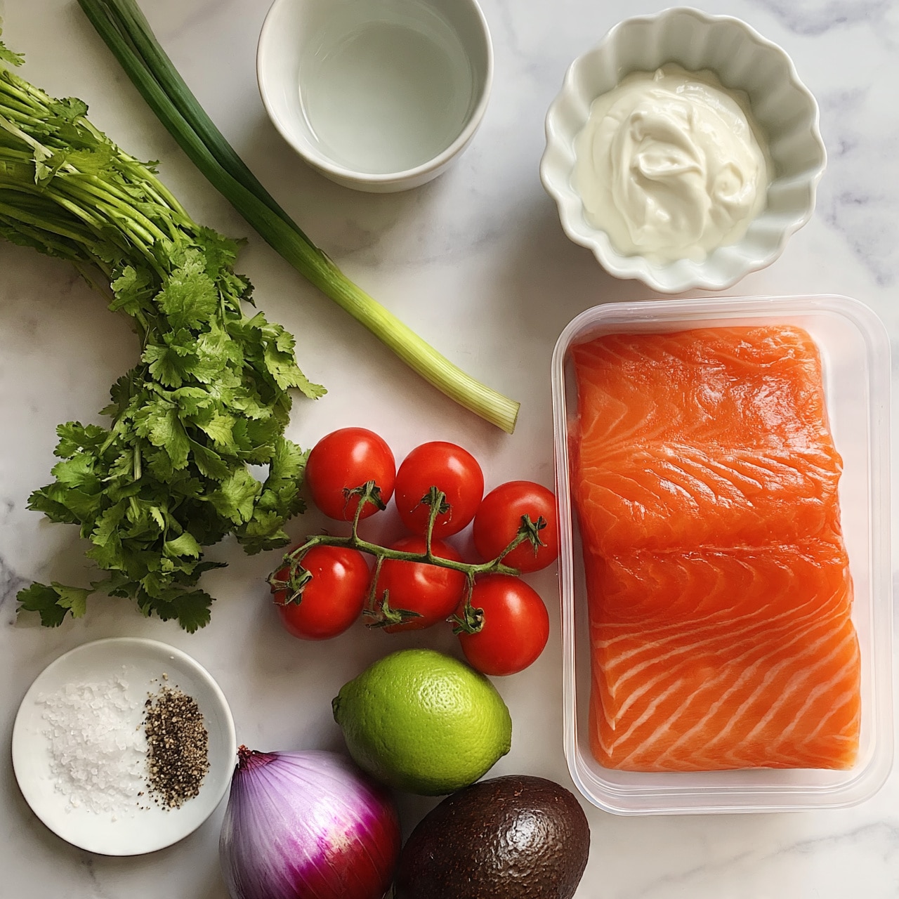 square image The image shows fresh ingredients on a white marbled surface. On the right side, there is a clear rectangular container holding a large piece of bright orange salmon with visible white lines of fat. Above the salmon, there is a small white scalloped bowl filled with creamy white sauce. Near the top center, a small white bowl contains clear liquid, likely oil. To the left, there is a long bunch of green cilantro and a single green onion lying horizontally. A cluster of bright red cherry tomatoes on the vine is placed below the greens. At the bottom left corner, a small white plate holds coarse salt and pepper. Below it, a whole lime with a green rind, a purple-red onion, and a dark brown avocado complete the layout. The colors are fresh and vibrant, contrasting softly with the white marbled texture background. photo taken with an iphone --ar 4:5 --v 7