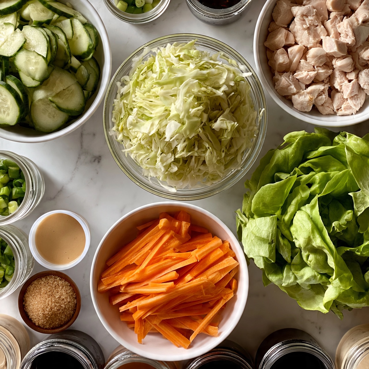 square image The image shows a white marbled surface with several bowls and small containers arranged neatly. At the top left, a white bowl contains thinly sliced cucumber with green skin and pale centers. In the center, there is a clear glass bowl filled with finely shredded pale green cabbage. To the top right, a white bowl holds small chunks of light pink cooked chicken. Below these, a white bowl with thin, bright orange carrot sticks is placed near a fresh, bright green butter lettuce head on the right. Around these main bowls, there are small glass jars with chopped green onions, a small white container with a light tan sauce, a small brown bowl with granulated brown sugar, and containers with various dark and light sauces arranged neatly across the surface. photo taken with an iphone --ar 4:5 --v 7