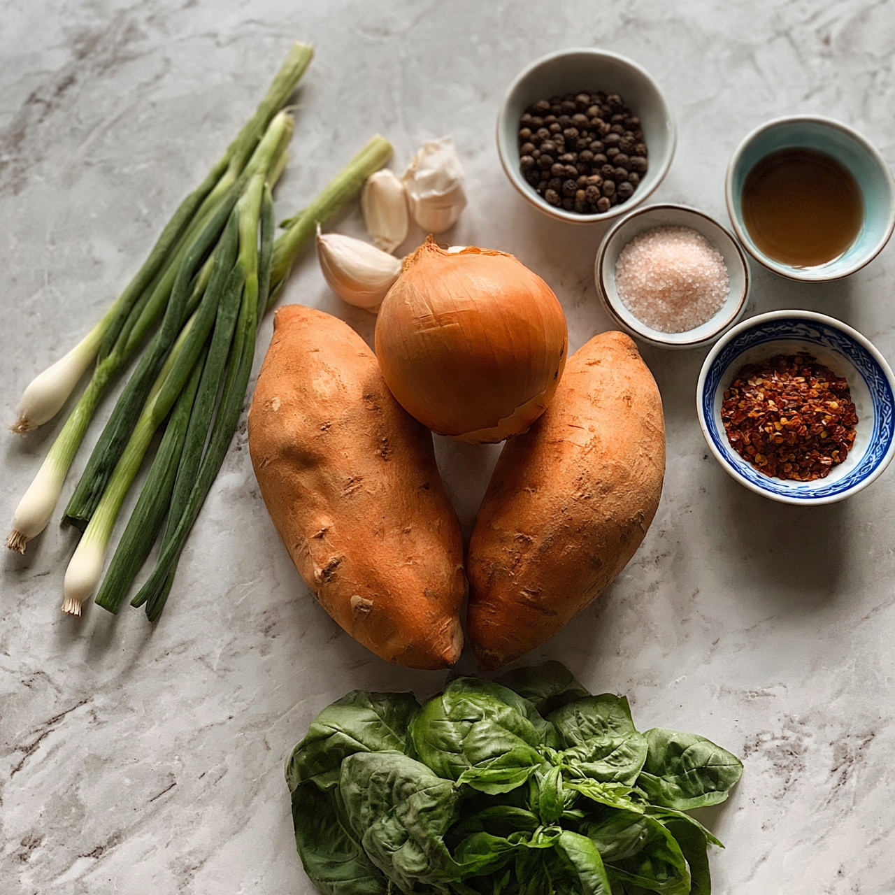 square image The image shows a collection of fresh ingredients arranged on a white marbled surface. In the center, there are two large orange sweet potatoes with rough skin, accompanied by a round, brown onion positioned above them. To the left, three green onions with white bulbs and long green stalks lie flat. Three garlic cloves are placed just above the sweet potatoes. On the right side, there are four small bowls holding various spices and liquids: one bowl contains whole black peppercorns, another has a light pink salt, a third one holds a brownish liquid, and the last bowl features red chili flakes decorated with blue patterns on the sides. At the bottom, a cluster of fresh green basil leaves adds color contrast. The scene is evenly lit, highlighting textures and colors clearly. Photo taken with an iphone --ar 4:5 --v 7