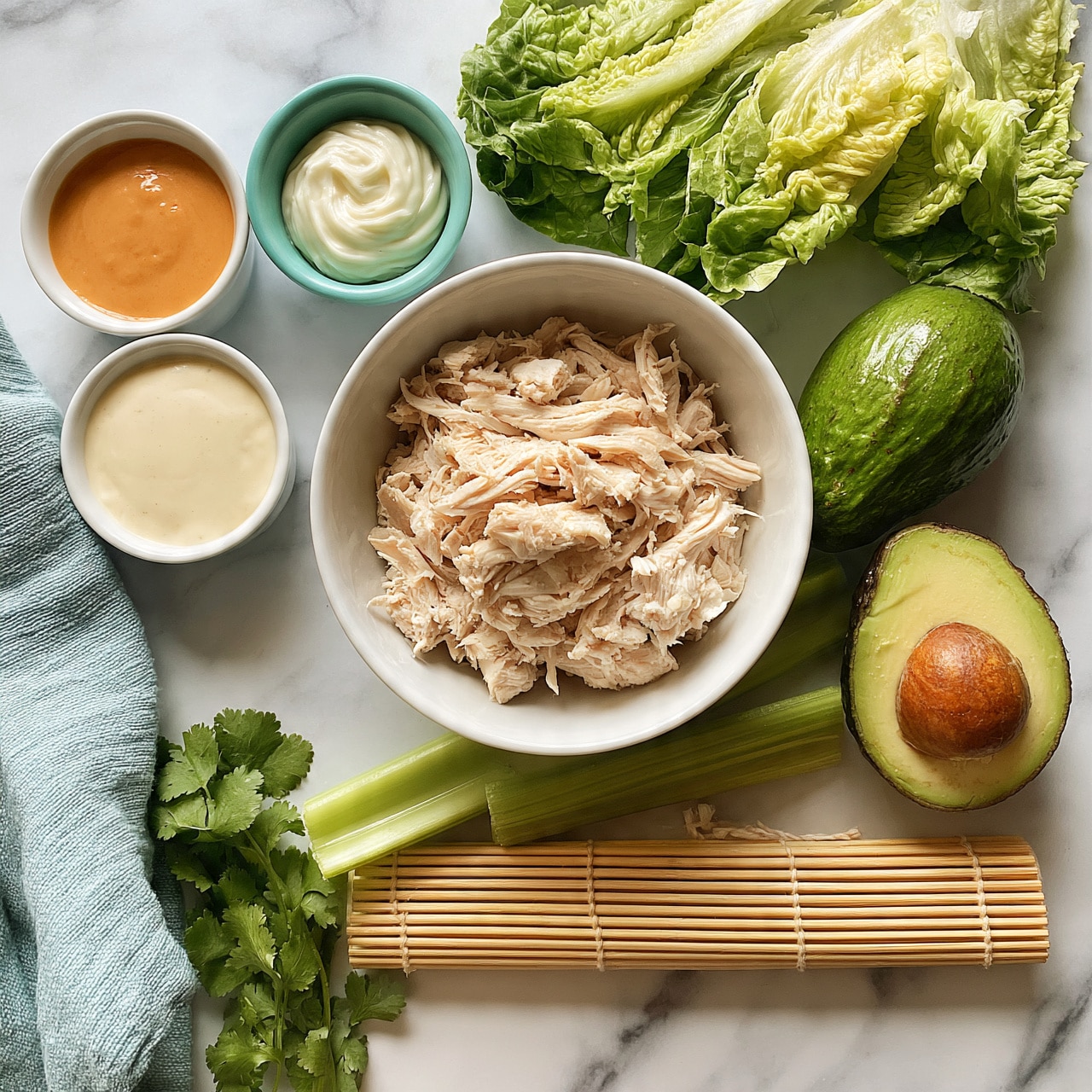 square image The image shows a top view of a white bowl filled with shredded cooked chicken, placed on a white marbled surface. Around the bowl, there are three small white bowls with different sauces: a smooth orange sauce, a creamy white sauce, and a swirl of thicker white sauce in a teal bowl. To the top right of the bowl, fresh romaine lettuce leaves are arranged. Below the lettuce, a whole avocado and a half avocado with its brown seed are placed side by side. Two green celery stalks lay horizontally under the bowl, and a bamboo sushi rolling mat is horizontally placed beneath the celery. Green cilantro sprigs and a folded light blue cloth napkin are arranged on the left side of the image. Photo taken with an iphone --ar 4:5 --v 7