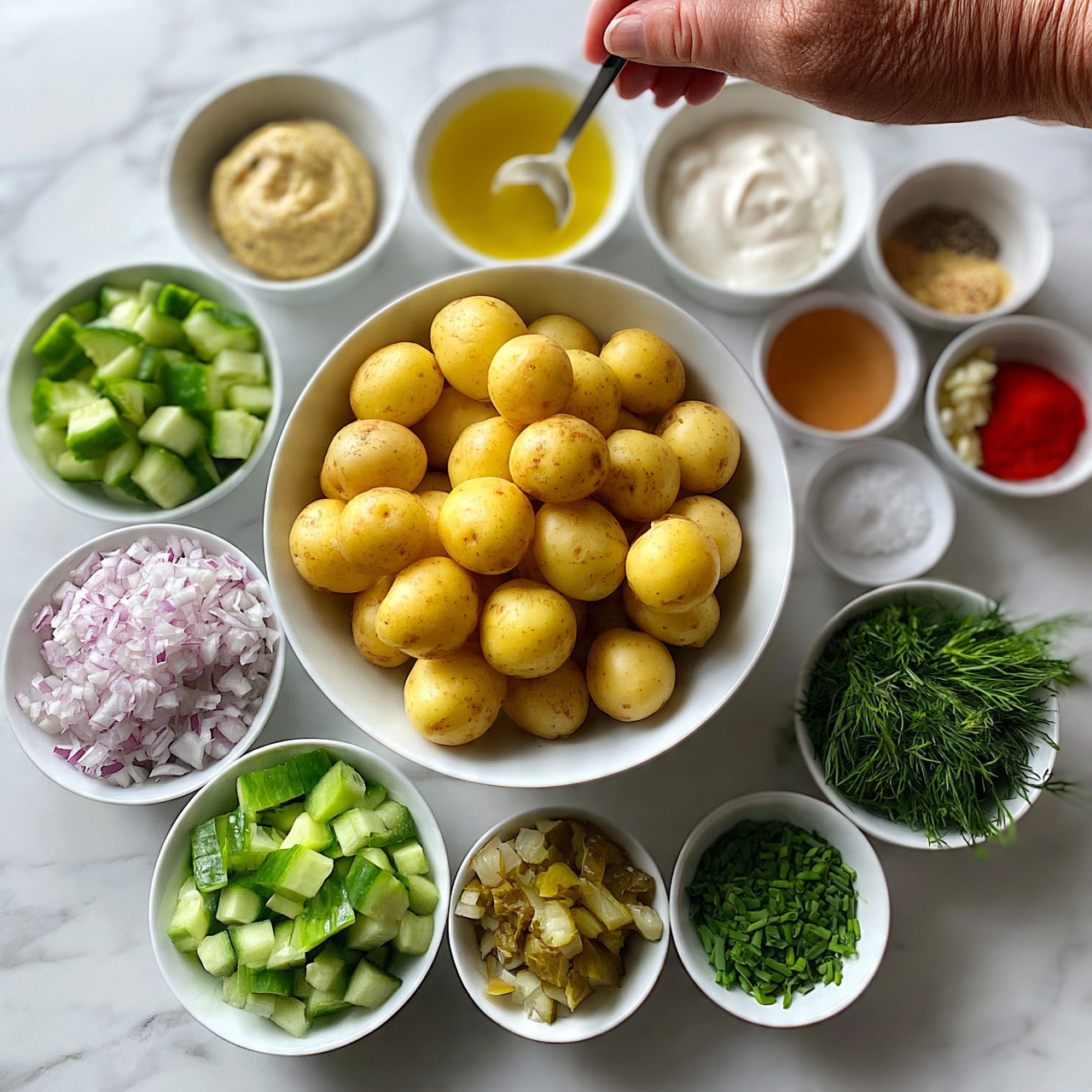 square image The image shows a white bowl filled with many small round yellow potatoes at the center. Around the bowl, there are smaller white bowls with different fresh ingredients: diced cucumber with bright green skins and pale green inside, finely chopped red onions showing light purple color, chopped pickles with a mix of light and dark green, fresh green dill leaves, and chopped chives. There are also small white bowls containing light yellow mustard, yellow vinegar, white sour cream, a golden yellow liquid, a light reddish liquid, salt, black pepper, minced garlic, and two bowls with mixed spices in light brown and bright red colors. The bowls are arranged neatly on a white marbled surface, and a woman's hand is holding a spoon above some ingredients. photo taken with an iphone --ar 4:5 --v 7