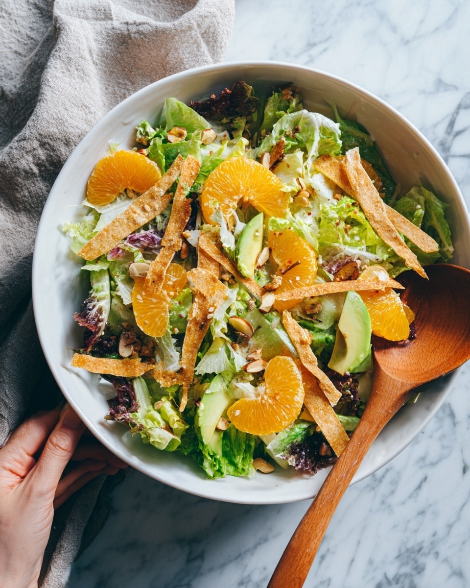 A white bowl filled with a fresh salad showing multiple layers, starting with a base of mixed dark and light green leafy lettuce. Scattered on top are bright orange mandarin slices adding a juicy and vibrant pop of color. Thin tan strips of toasted tortilla are spread evenly over the salad, providing a crunchy texture. There are also light green slices of avocado and small bits of nuts sprinkled throughout for extra detail and texture. Around the bowl part of a woman's hand holding a wooden utensil with a white marbled surface underneath. Photo taken with an iphone --ar 4:5 --v 7