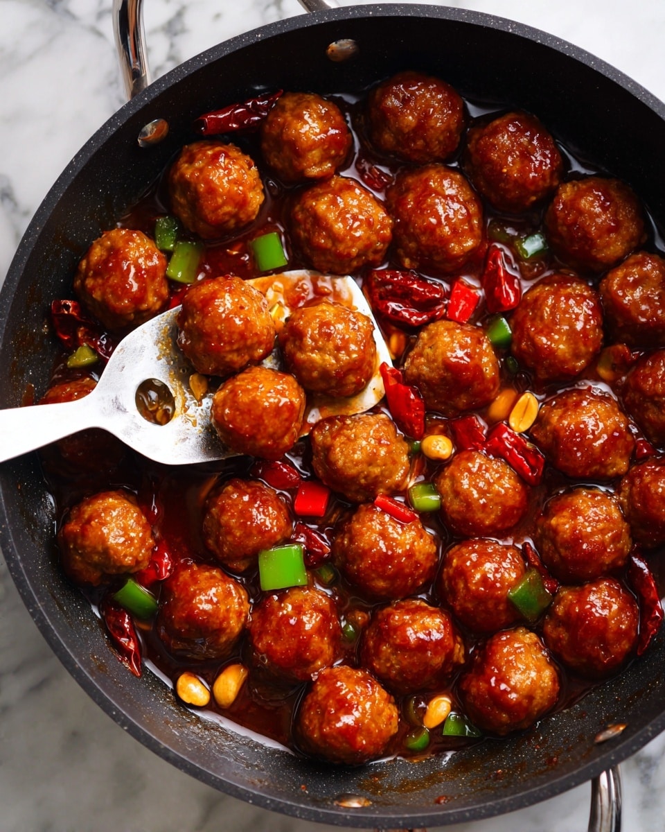 A black pan filled with round, golden-brown meatballs coated in a shiny reddish-brown sauce. Scattered around the meatballs are small pieces of green and red bell peppers, dried red chili peppers, and light brown peanuts. A silver spatula lifts one meatball, showing its glossy texture. The surface beneath the pan has a white marbled texture. photo taken with an iphone --ar 4:5 --v 7