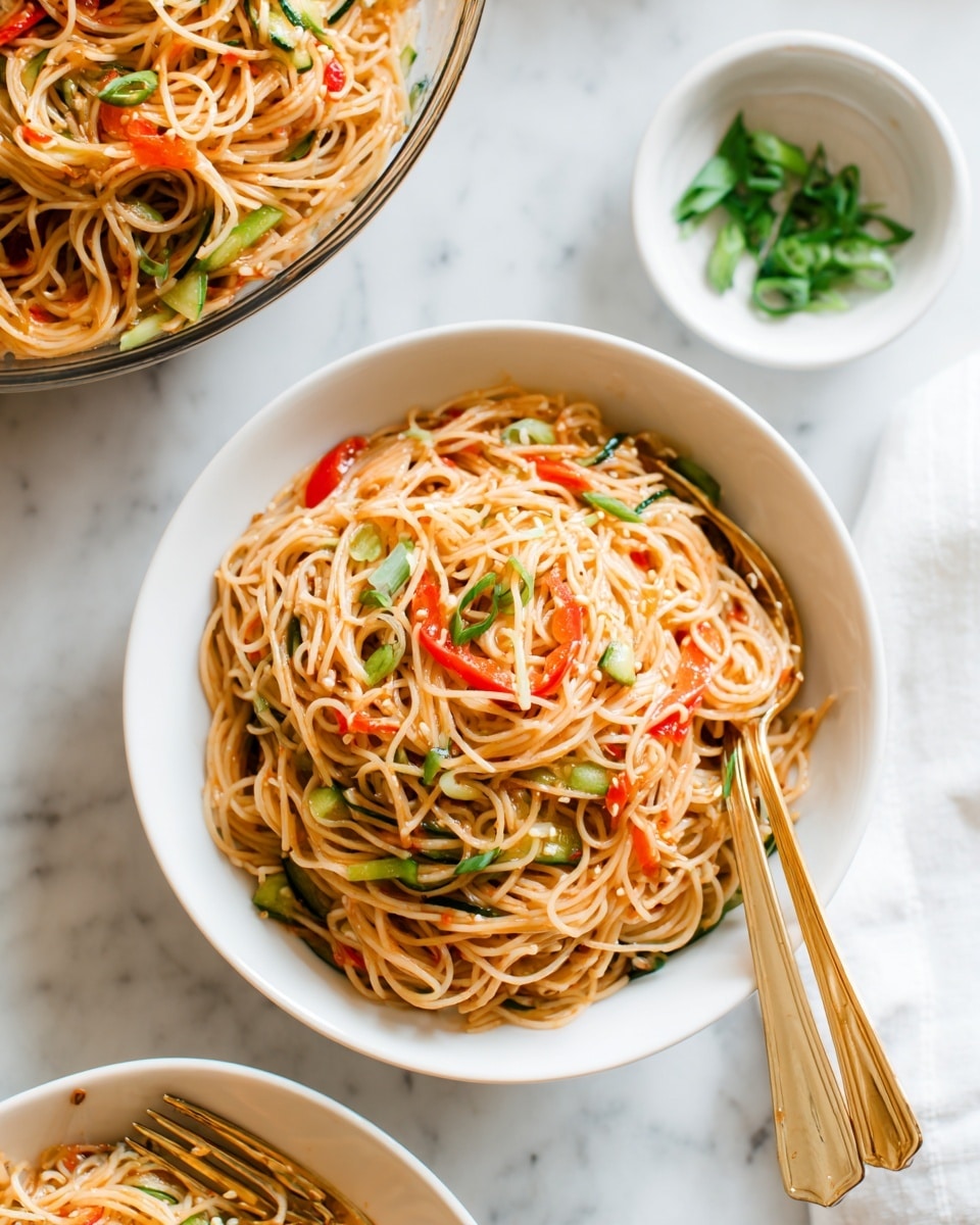 A white bowl filled with thin noodles mixed with small pieces of green cucumber and red bell pepper, with light brown sauce coating the noodles, placed on a white marbled surface. Above, a larger glass bowl holds more of the same noodle salad. To the right, a small white bowl contains chopped green onions. Two gold utensils rest near the bowls on the white marbled surface. photo taken with an iphone --ar 4:5 --v 7