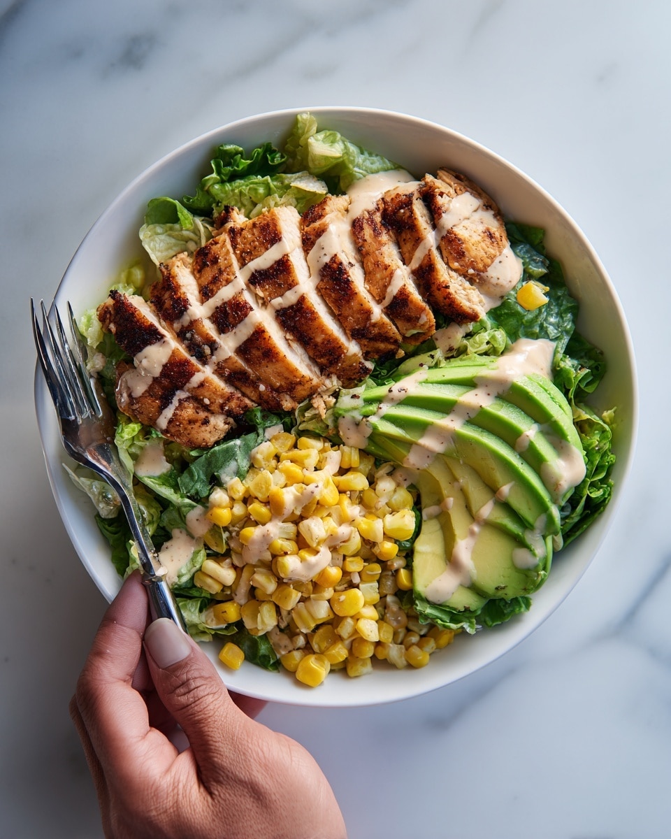 A white bowl on a white marbled surface holds a salad with layered ingredients: at the bottom is a bed of green lettuce mixed with other greens, on top left are thick slices of grilled chicken with a golden-brown, slightly charred texture. To the right of the chicken are fresh, sliced avocado pieces with a smooth, creamy green color. Next to the avocado, sweet corn kernels with a bright yellow hue are scattered. The dish is topped with a light drizzle of creamy dressing. A woman's hand holds a fork on the left side of the bowl. Photo taken with an iphone --ar 4:5 --v 7