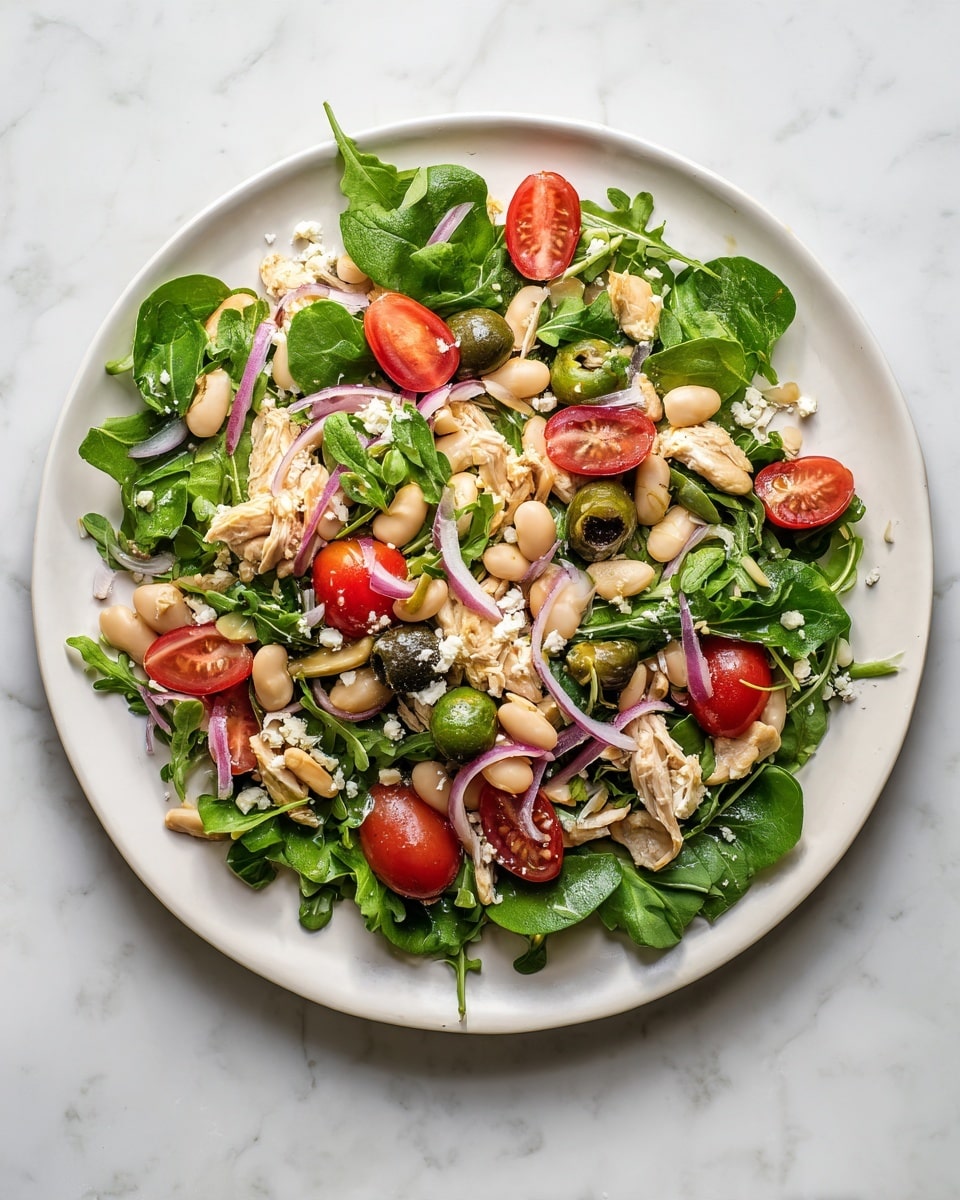 A white plate holds a fresh salad on a white marbled surface. The bottom layer is made of green arugula leaves scattered around. Above that, there are white beans and green olive slices spread evenly throughout. Red cherry tomato halves and thin slices of purple onion are added on top, giving bright pops of color. There are also small pieces of light-colored chicken mixed in. Tiny white crumbles of cheese are sprinkled over the salad. The salad looks fresh and colorful, with a variety of textures from soft beans, crisp greens, juicy tomatoes, and tender chicken. photo taken with an iphone --ar 4:5 --v 7