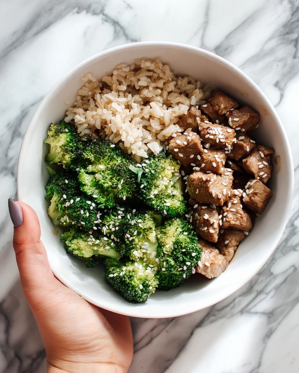 A white bowl filled with a dish that has three main layers: at the bottom, cooked brown rice with a slightly rough texture, in the middle, bright green broccoli florets that look steamed and fresh, and on top, pieces of cooked brown meat cut into small chunks, all sprinkled with white sesame seeds. A woman's hand is holding the bowl from the right side, and the whole scene is set on a white marbled surface. photo taken with an iphone --ar 4:5 --v 7