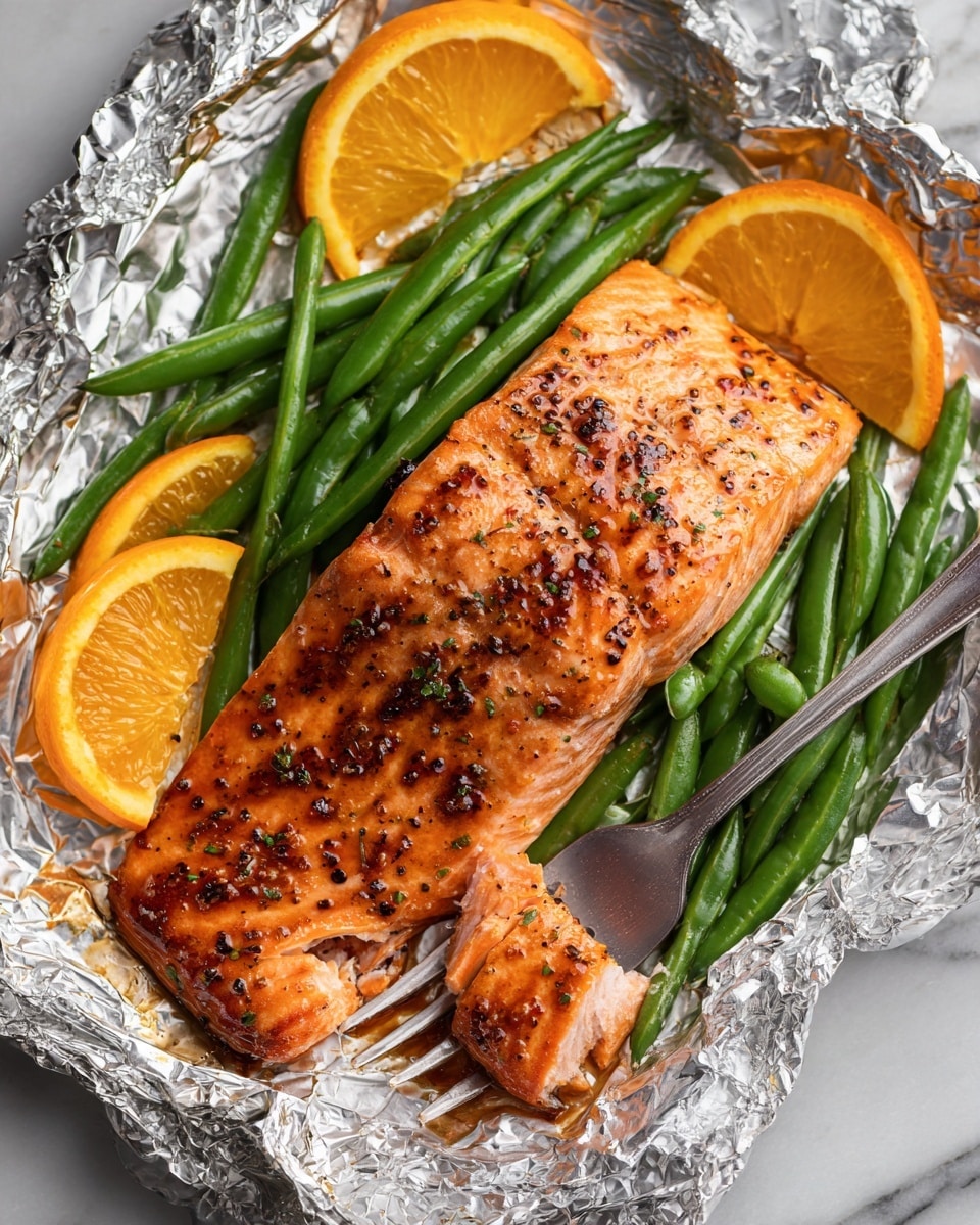 A piece of cooked salmon with a shiny, orange-brown color and black pepper on top sits in the center, surrounded by bright green snap peas and orange slices. The salmon has a tender texture showing a small piece flaked on a silver fork under it. The food is laid on shiny silver foil that crinkles around the edges, all set on a white marbled surface. photo taken with an iphone --ar 4:5 --v 7