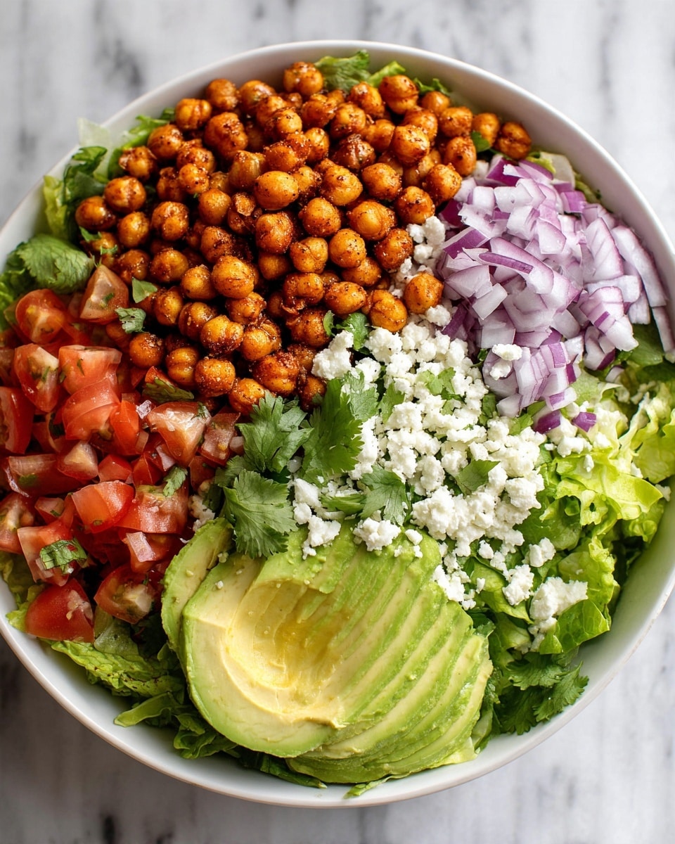 A white bowl filled with a layered salad on a white marbled surface. The base layer is fresh green lettuce and chopped tomato pieces. On top, there are roasted golden-brown chickpeas spread evenly, followed by slices of pale green avocado. Scattered around are thin purple onion slices and fresh green cilantro leaves. White crumbled cheese is sprinkled on the top, adding a creamy texture. The colors are vibrant with green, red, purple, white, and golden brown. Photo taken with an iphone --ar 4:5 --v 7