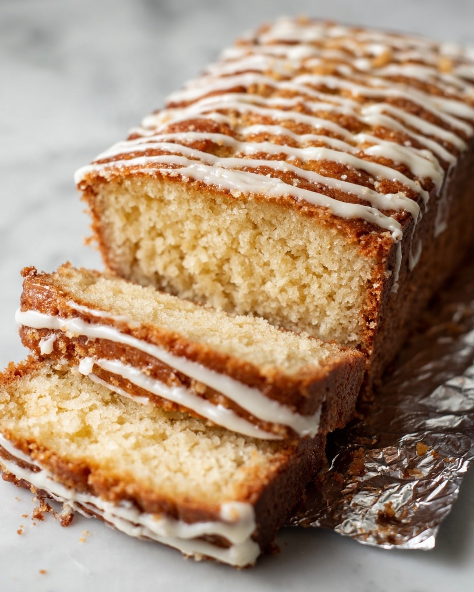 A close-up of a loaf cake sliced on the side to show four thick layers with a crumbly brown texture. The top layer has a drizzled white icing in thin lines, creating a soft contrast with the golden-brown crust. The cake appears moist with a slightly rough surface and visible small crumbs. The slices lie on a shiny silver foil that reflects light softly. The background is a white marbled texture. Photo taken with an iphone --ar 4:5 --v 7