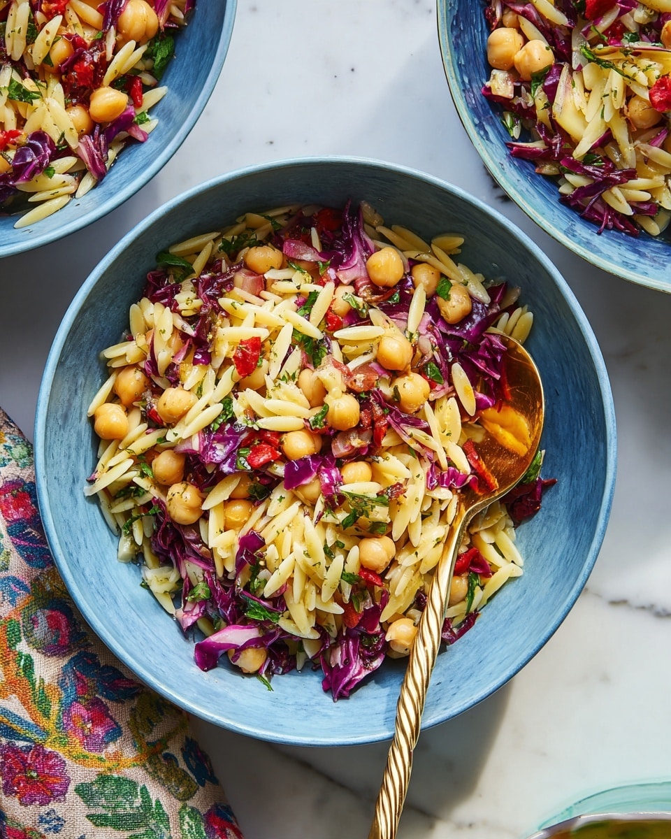 A blue bowl filled with a colorful mix of small, pale yellow orzo pasta stirred with round, golden chickpeas, scattered with chopped dark red radicchio, bright green herbs, and small pieces of red peppers. A shiny twisted gold spoon rests inside the bowl on the right side, pressing slightly into the food. The bowl is placed on a white marbled surface with part of a patterned cloth napkin showing at the bottom left and glimpses of two more similar bowls partly visible on the left side. The overall look is fresh and vibrant with a mix of soft and crunchy textures. photo taken with an iphone --ar 4:5 --v 7